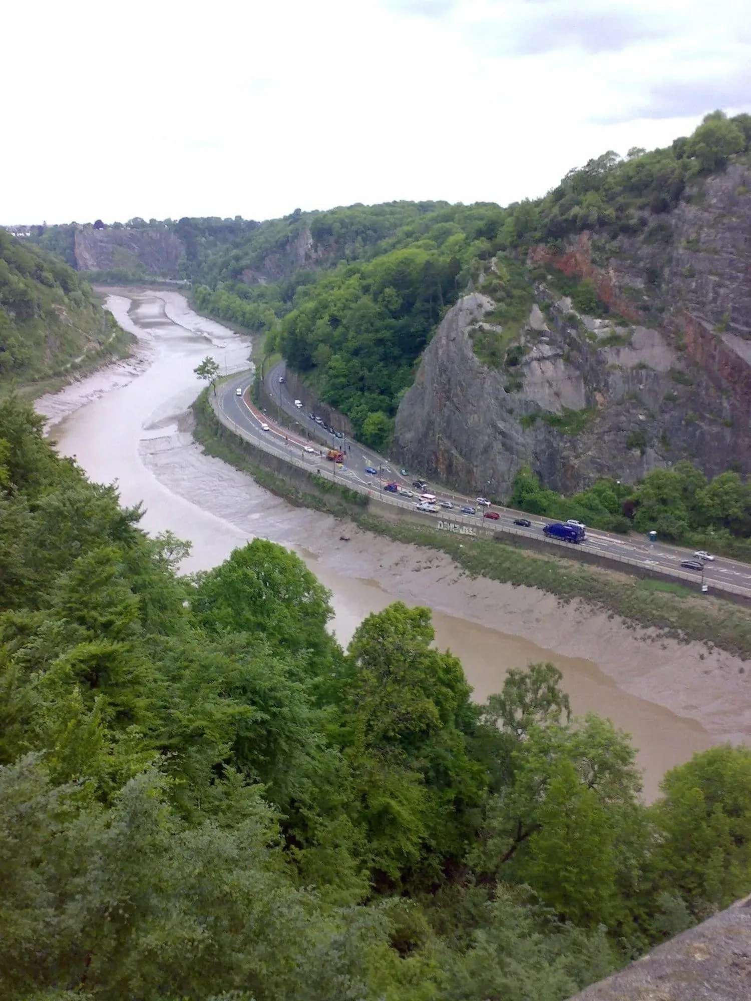 Elevated view of a winding river through forested gorge with highway carved into cliff face