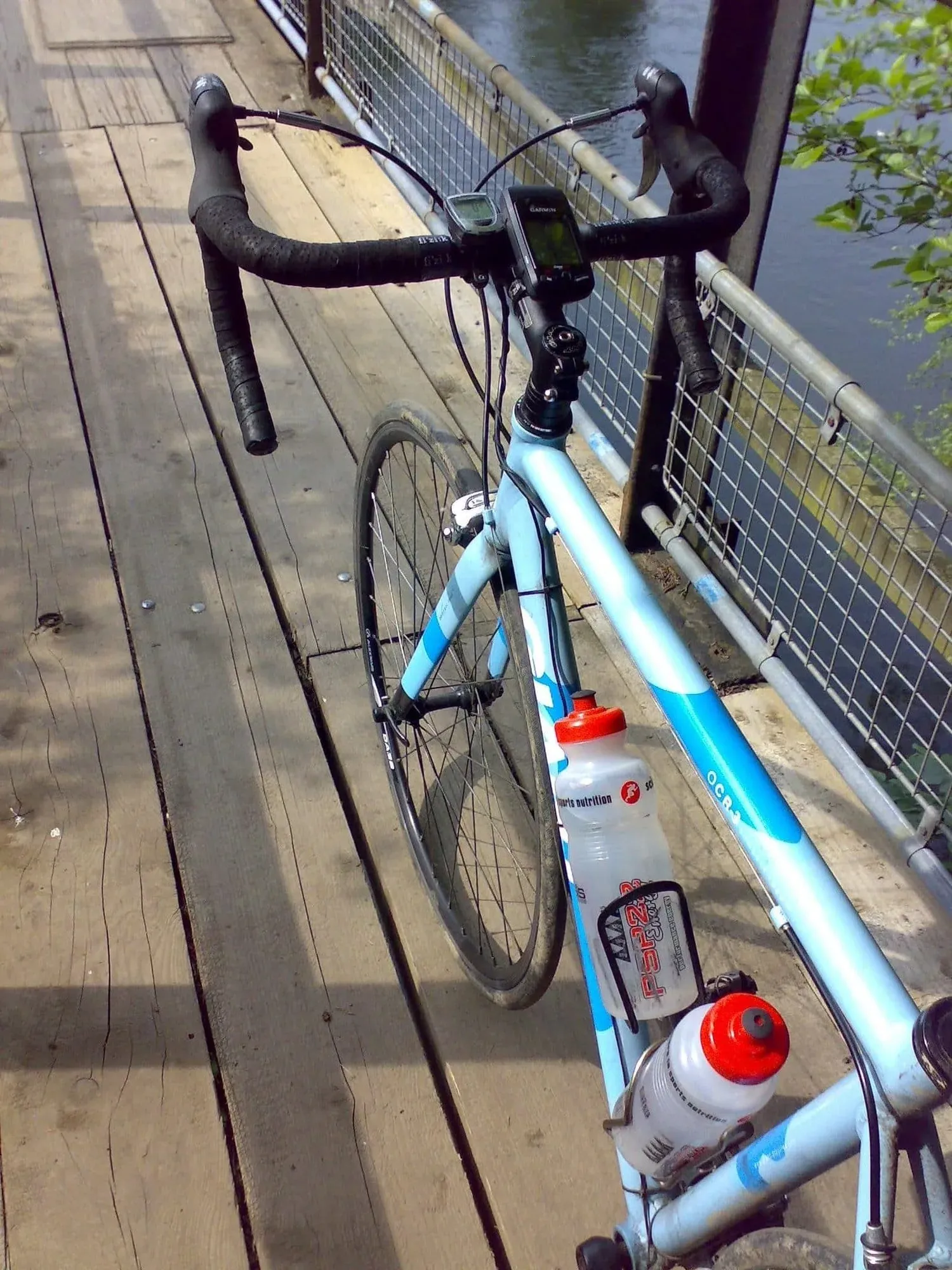 Blue road bike with water bottles on wooden bridge railing overlooking calm water