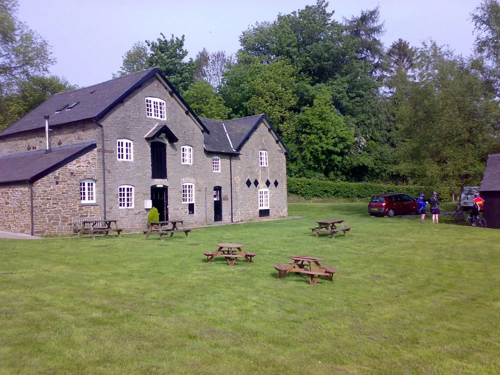 Stone building with multiple windows and picnic tables on grass, surrounded by trees