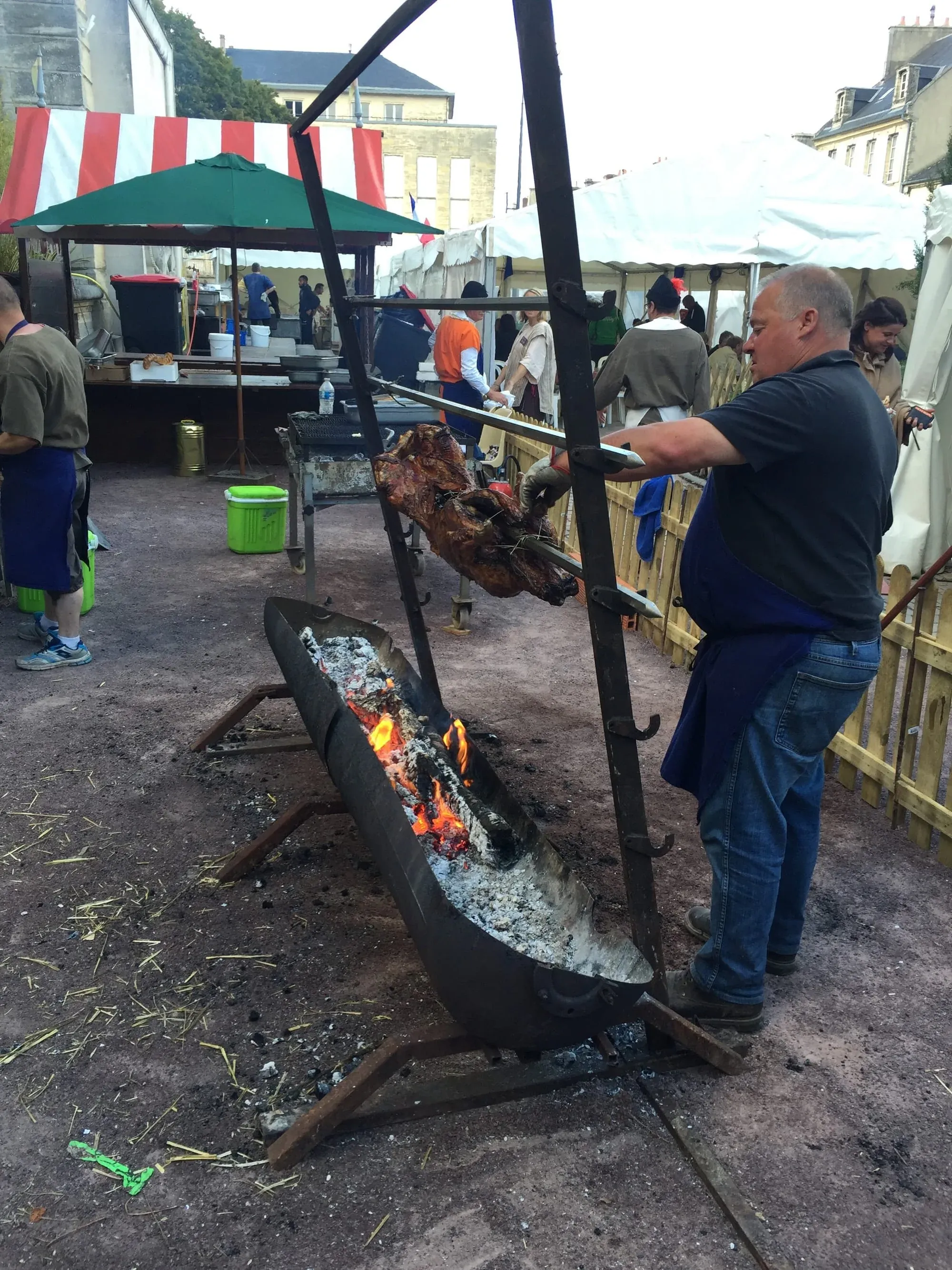 Man cooking meat over open campfire at outdoor festival with umbrellas
