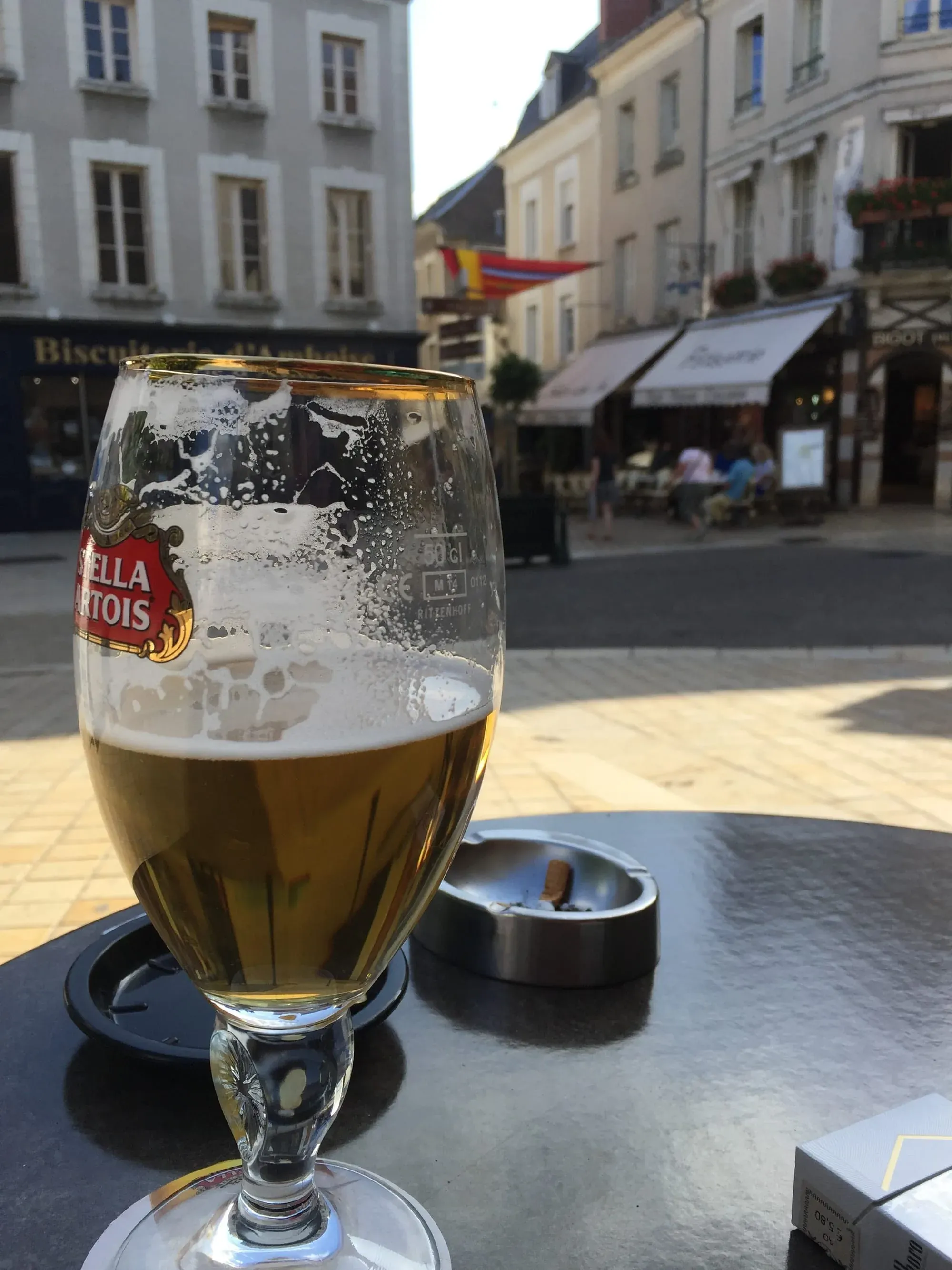 Glass of Stella Artois beer on outdoor café table in European town square