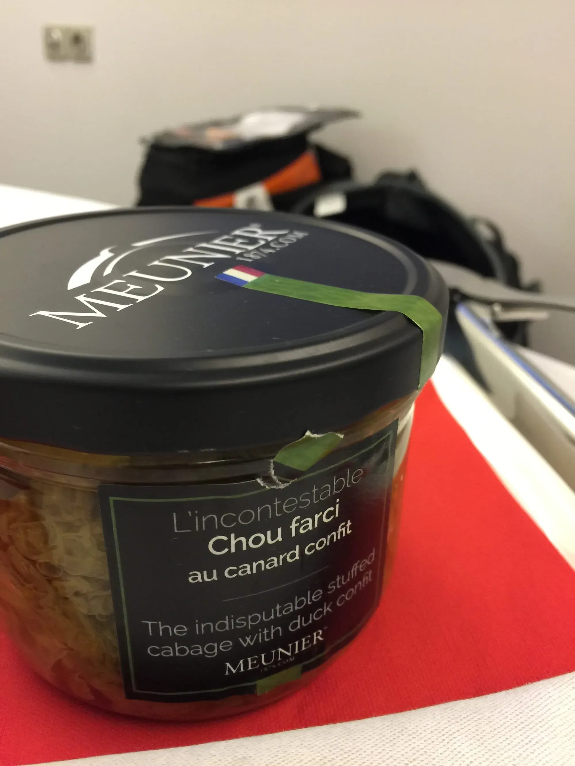 Jar of Meunier chou farci (stuffed cabbage) with duck confit on red surface