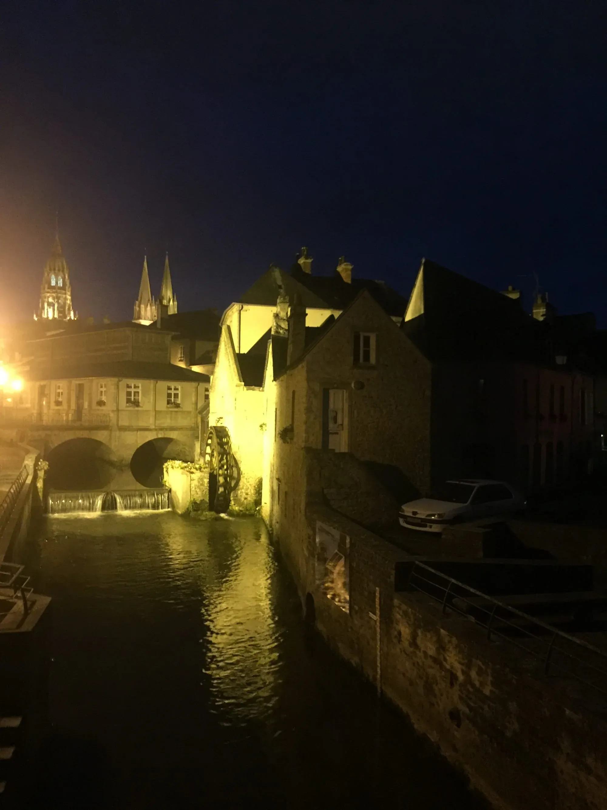 Illuminated medieval buildings and cathedral spires reflected in water at night