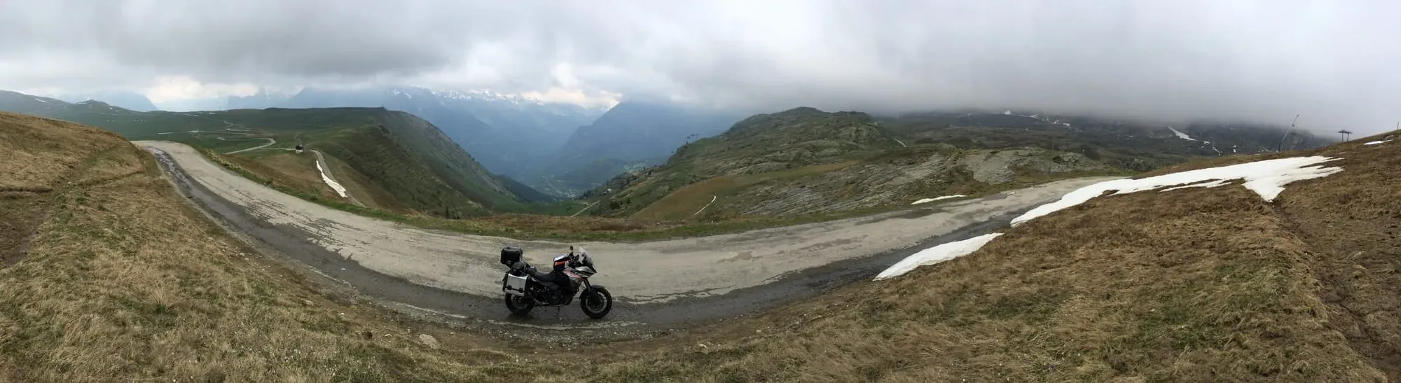 Motorcycle at high elevation plateau with snow patches and mountain valley backdrop