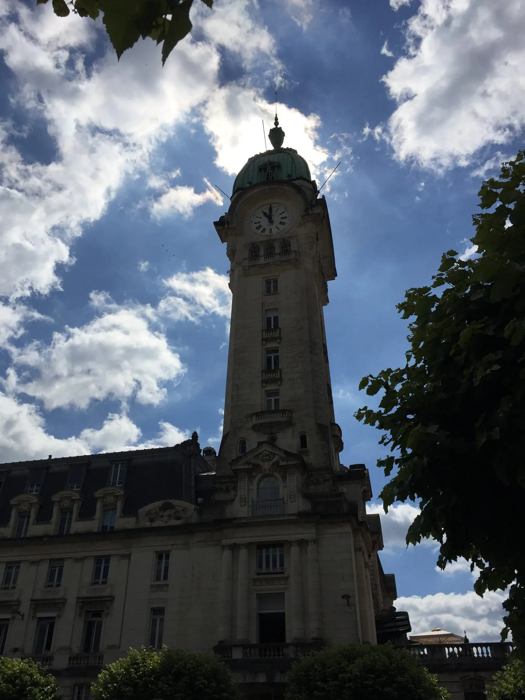 Tall clock tower with green dome against blue sky with white clouds