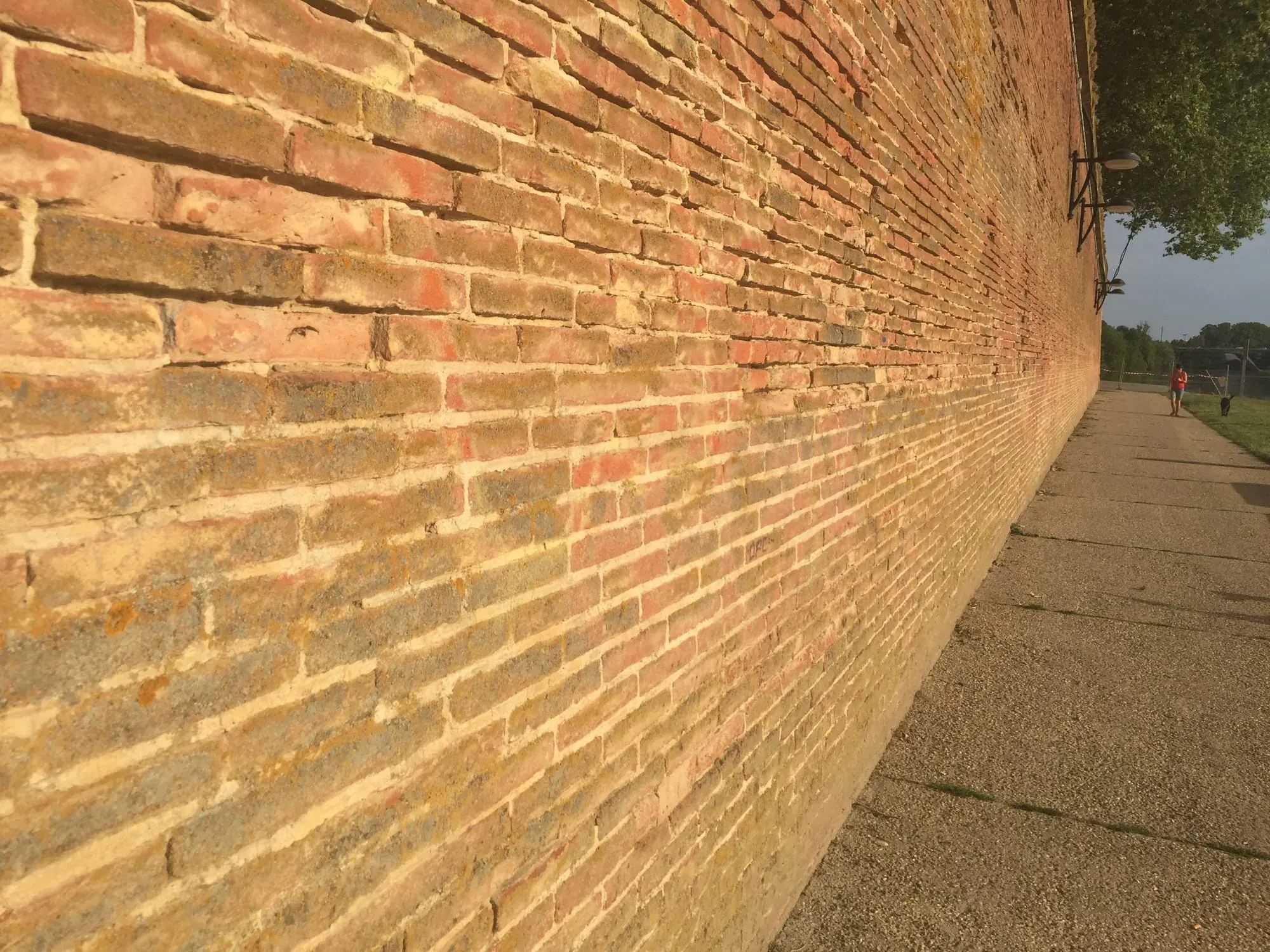 Red brick wall perspective receding into distance along paved pathway