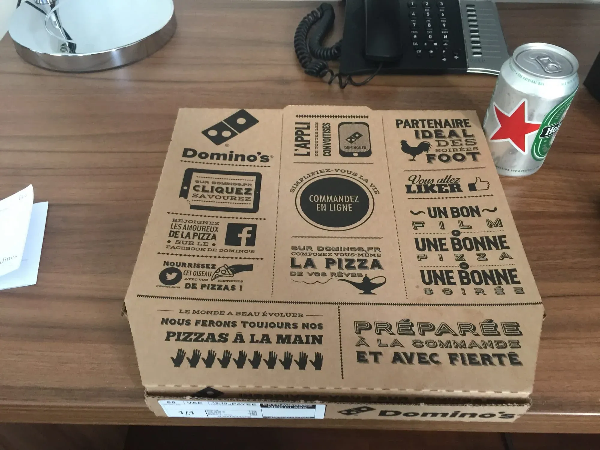 Domino's pizza box with French promotional text on wooden desk with office phone