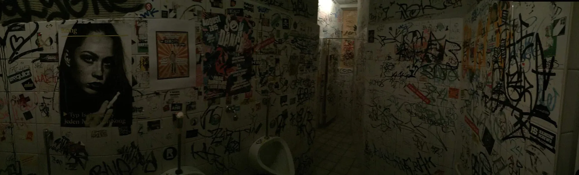 Graffiti-covered bathroom or utility room walls with various tags and stickers