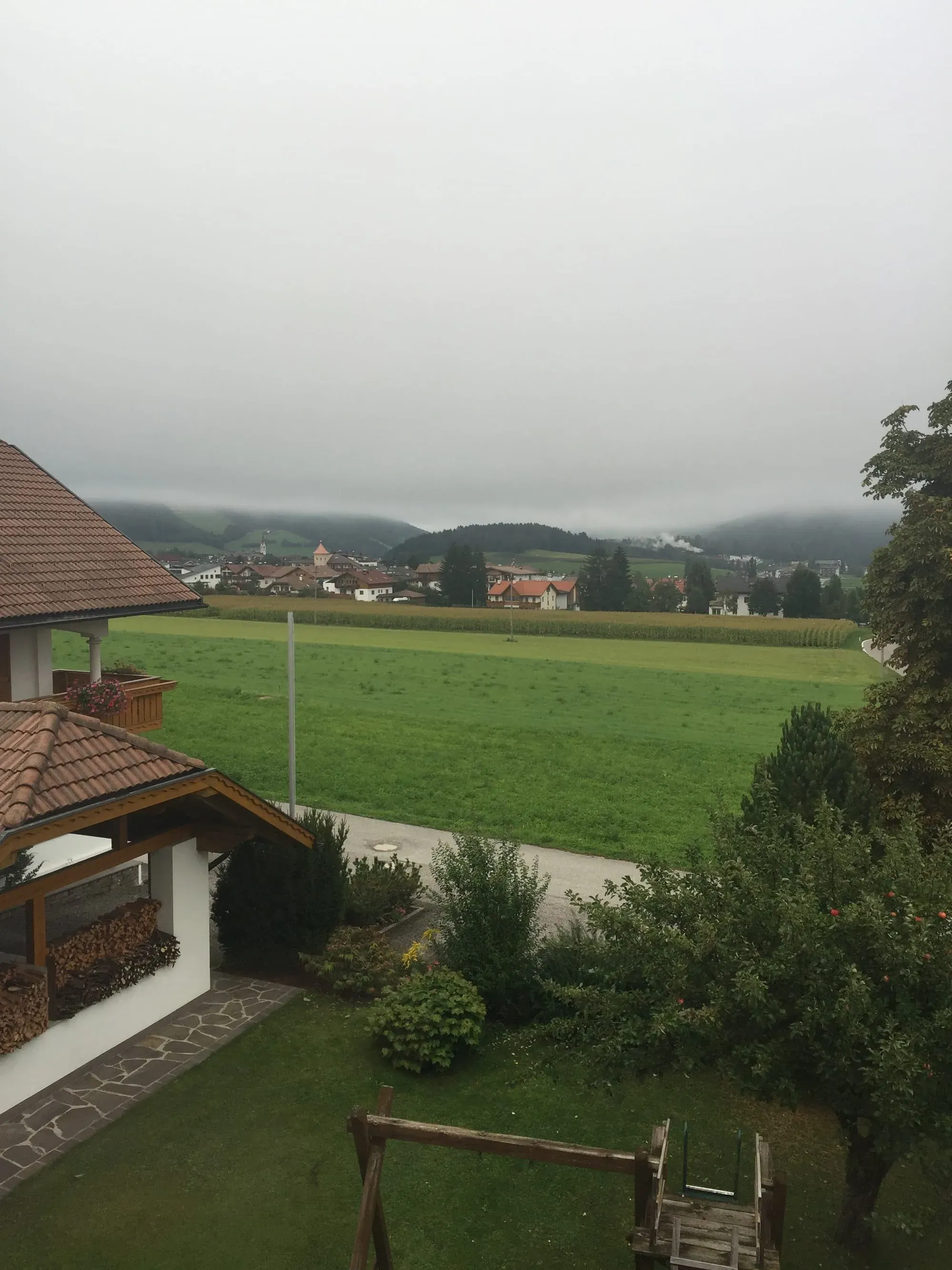 Alpine valley landscape with green meadows, village, and misty mountains