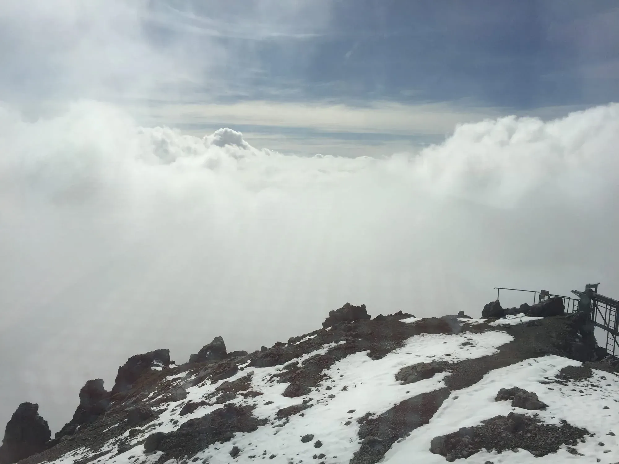 Rocky mountain summit with snow patches and observation platform overlooking clouds