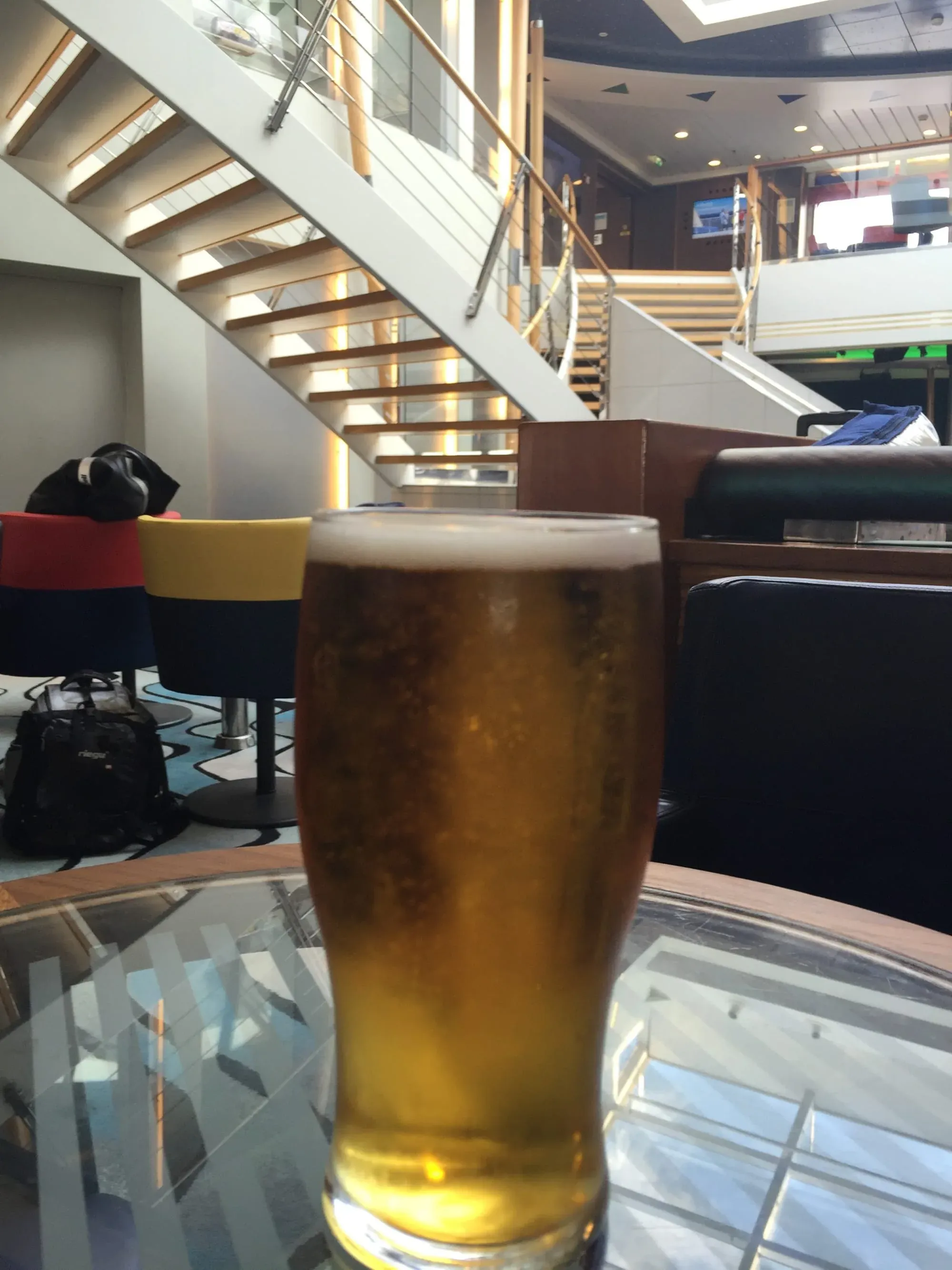Glass of beer on table in modern multi-level building interior with stairs