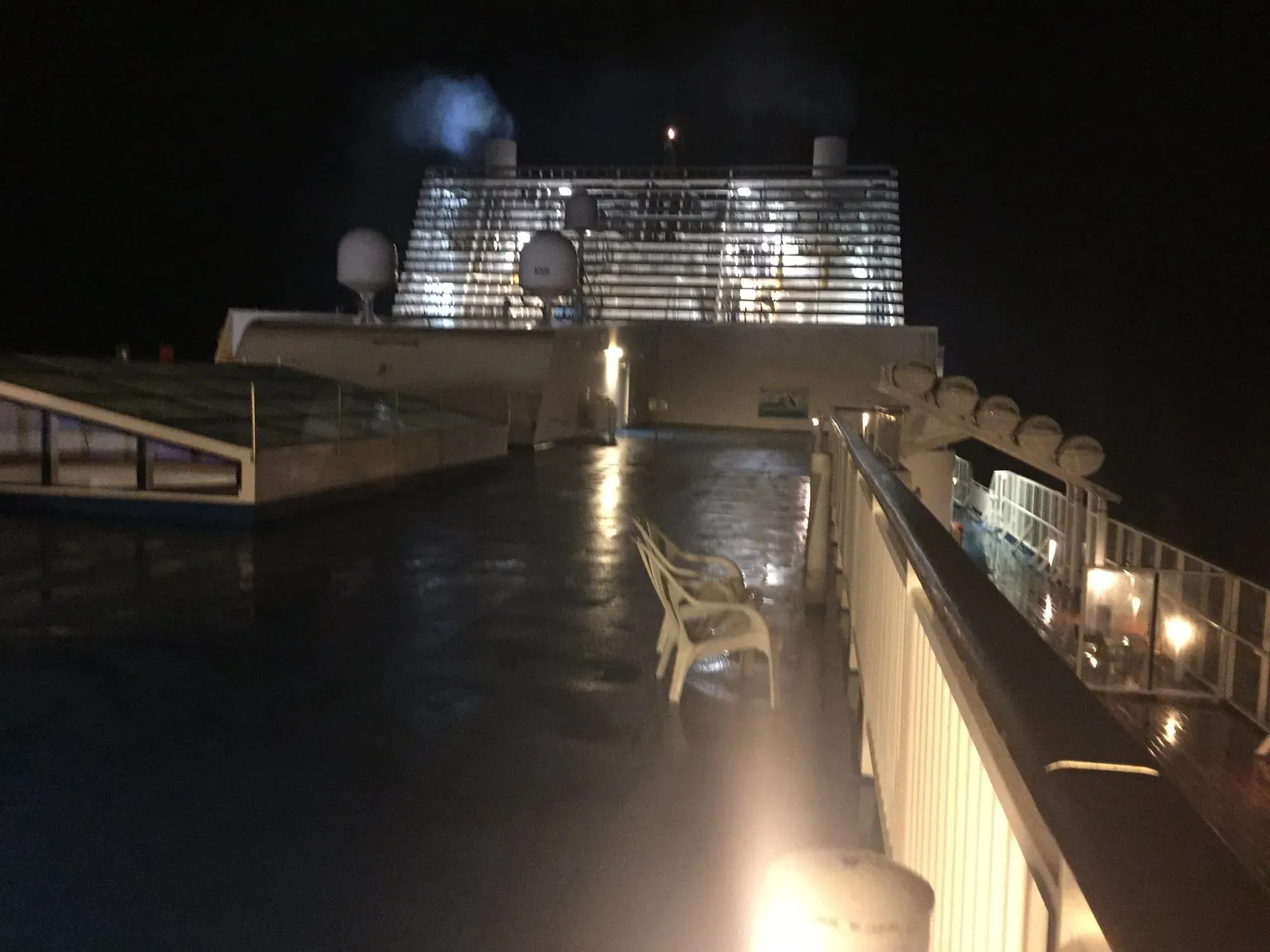 Wet ship deck at night with railings and deck furniture visible