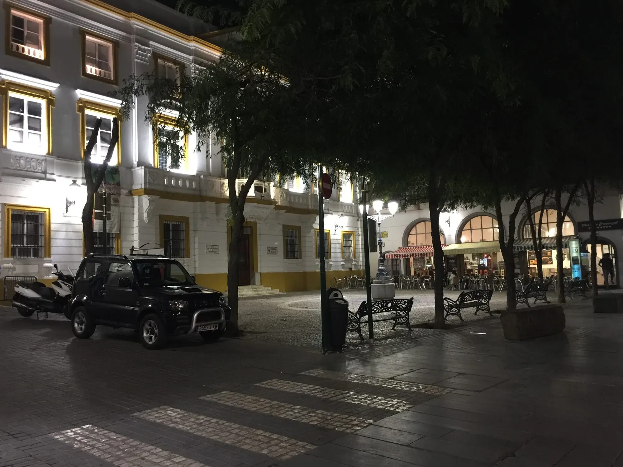 Illuminated colonial-style plaza with arched columns and tree-lined square at night