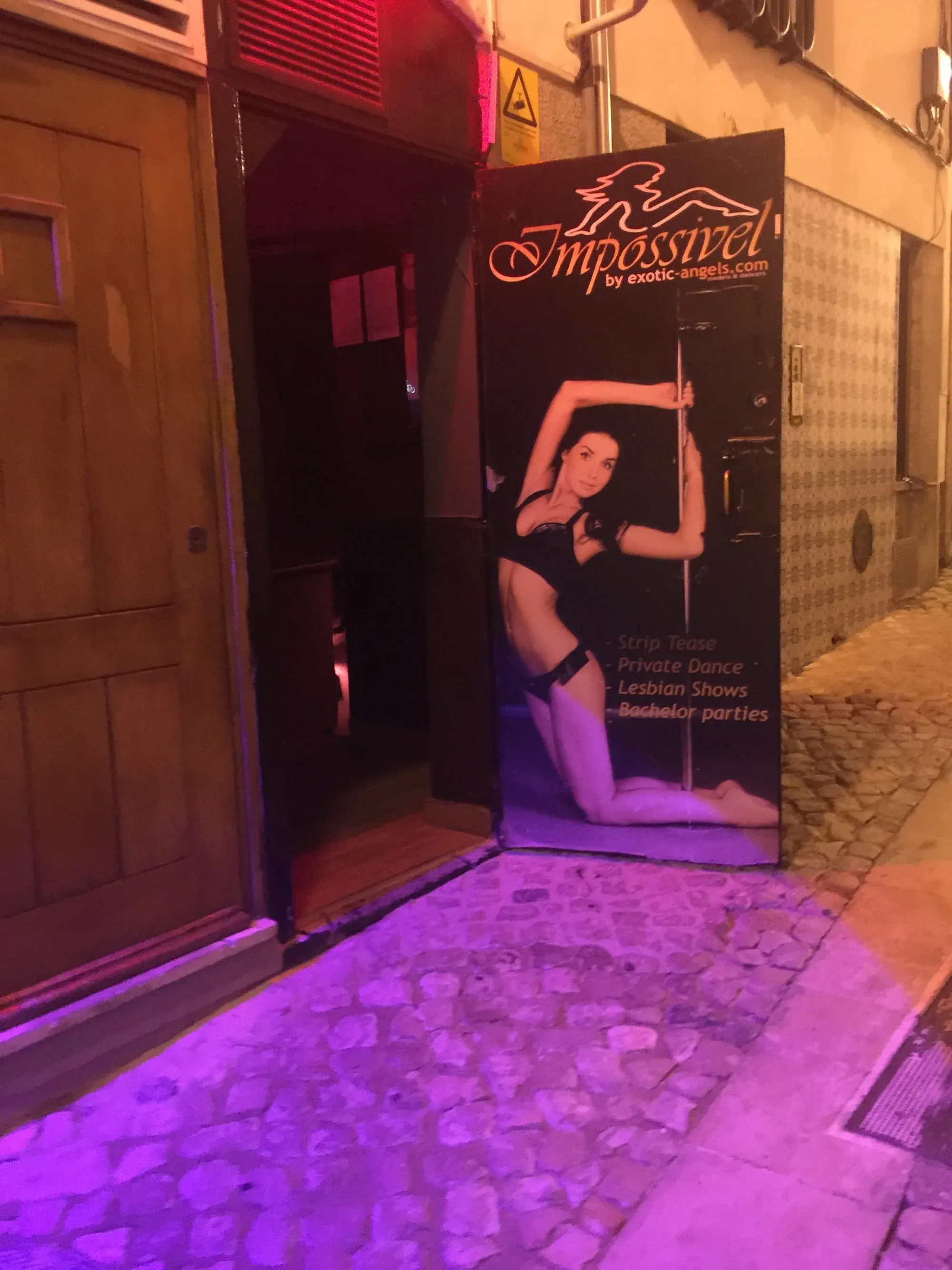 Neon-lit entrance to "Impossível" adult entertainment venue in narrow European street