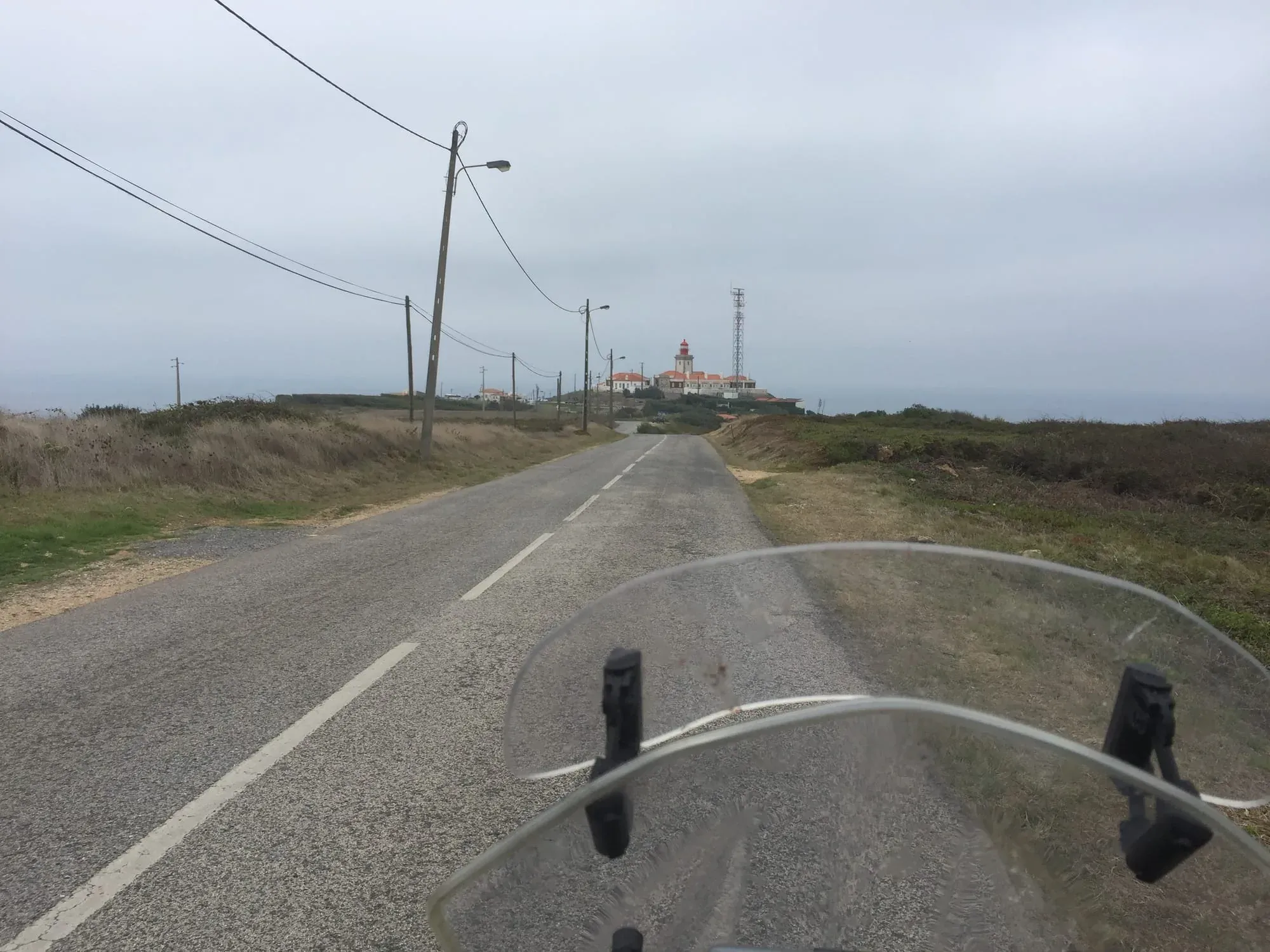 Motorcycle handlebar view of rural road with distant building and power lines