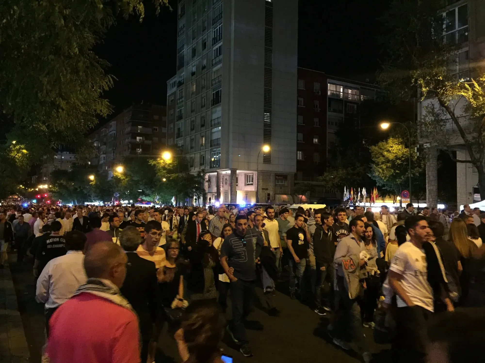 Crowded nighttime city plaza celebration with many people gathered under street lights