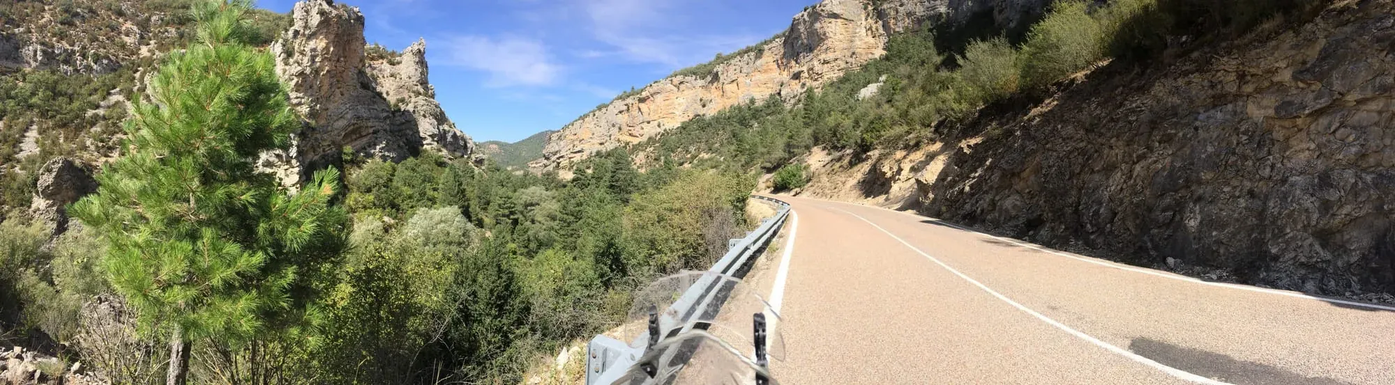 Motorcycle windshield view of winding mountain road through rocky canyon with guardrail