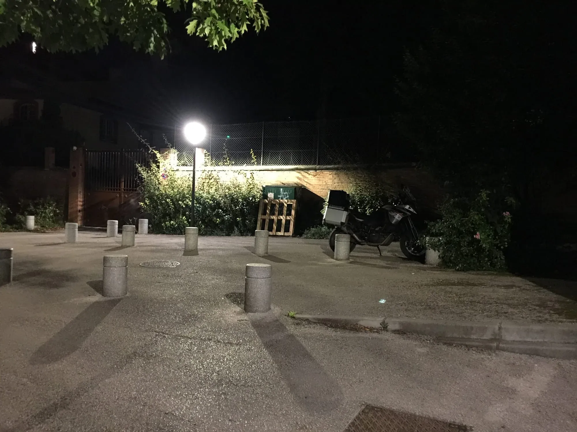 Dark motorcycle parked in concrete area under bright floodlight near fence