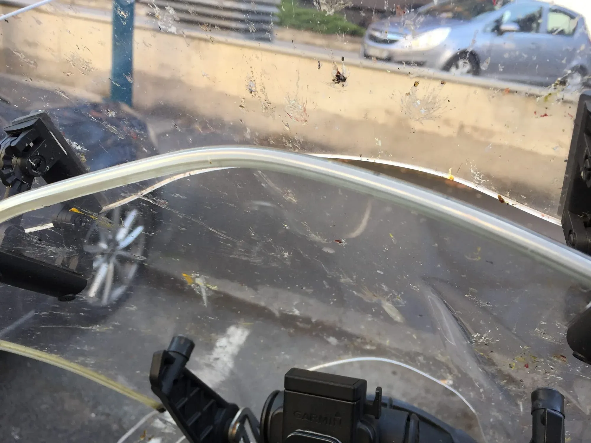 Dirty motorcycle windshield with view of sandy beach and parked cars