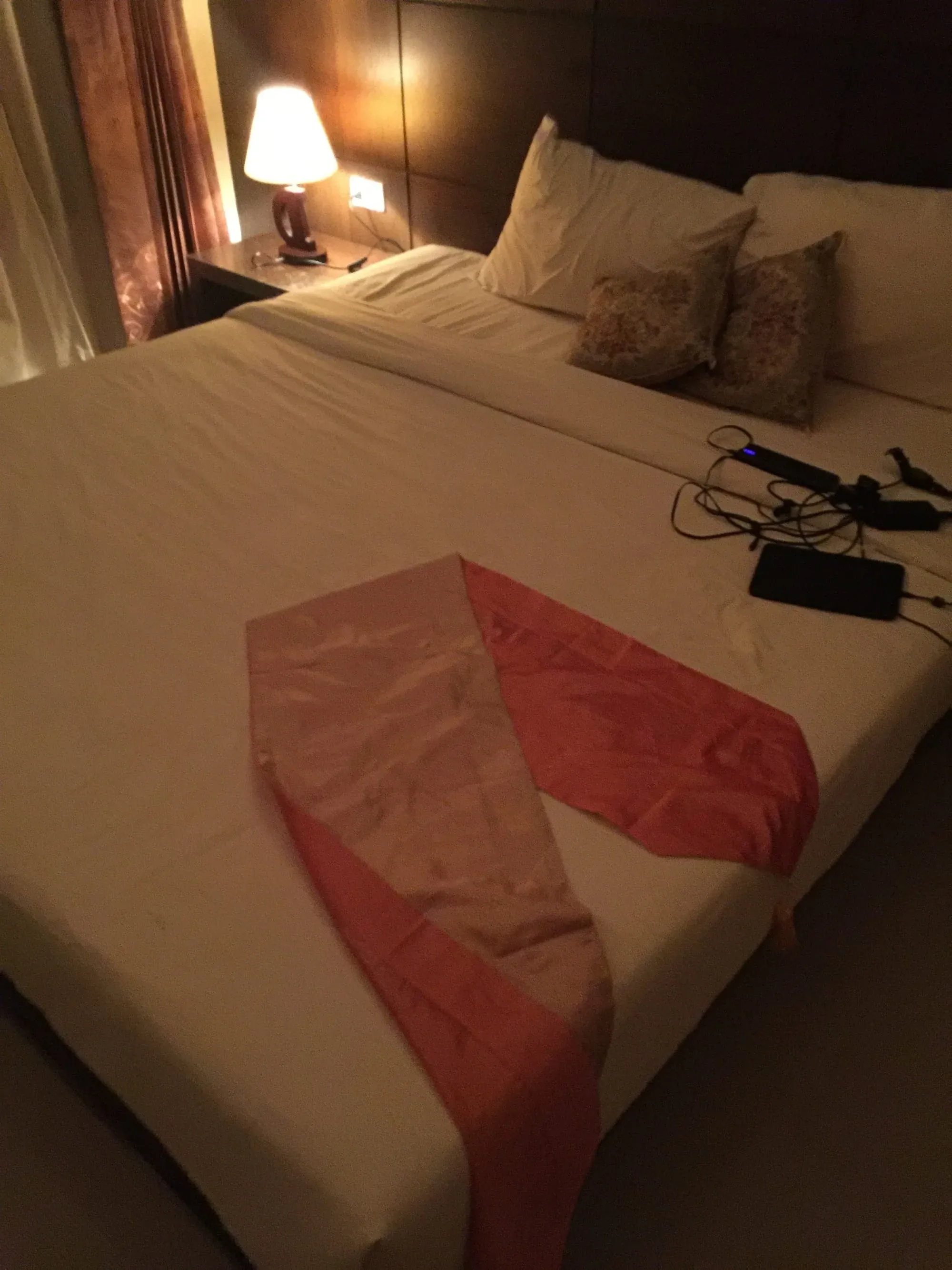 Hotel bed with red fabric decoration and charging cables