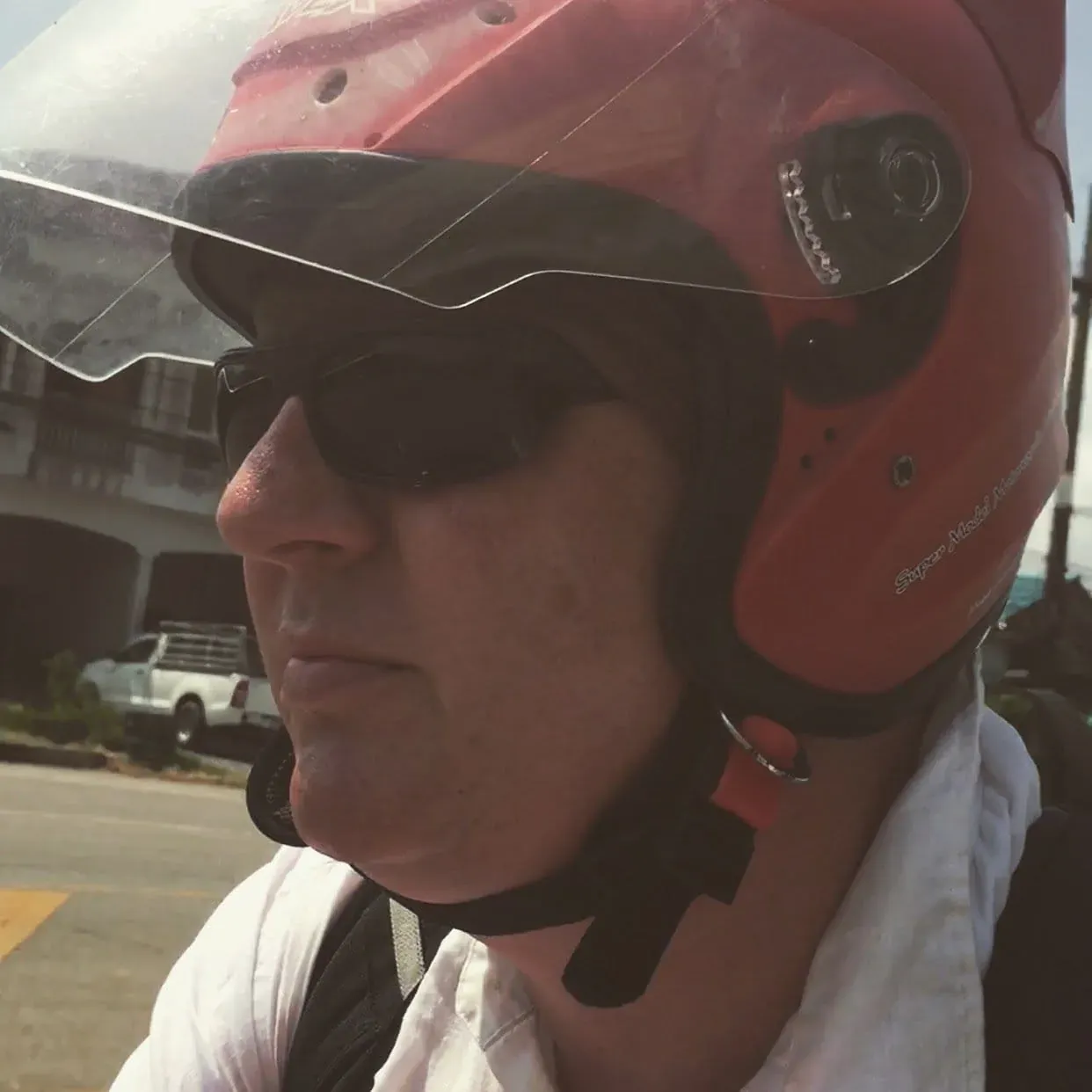 Person wearing red motorcycle helmet and sunglasses on street