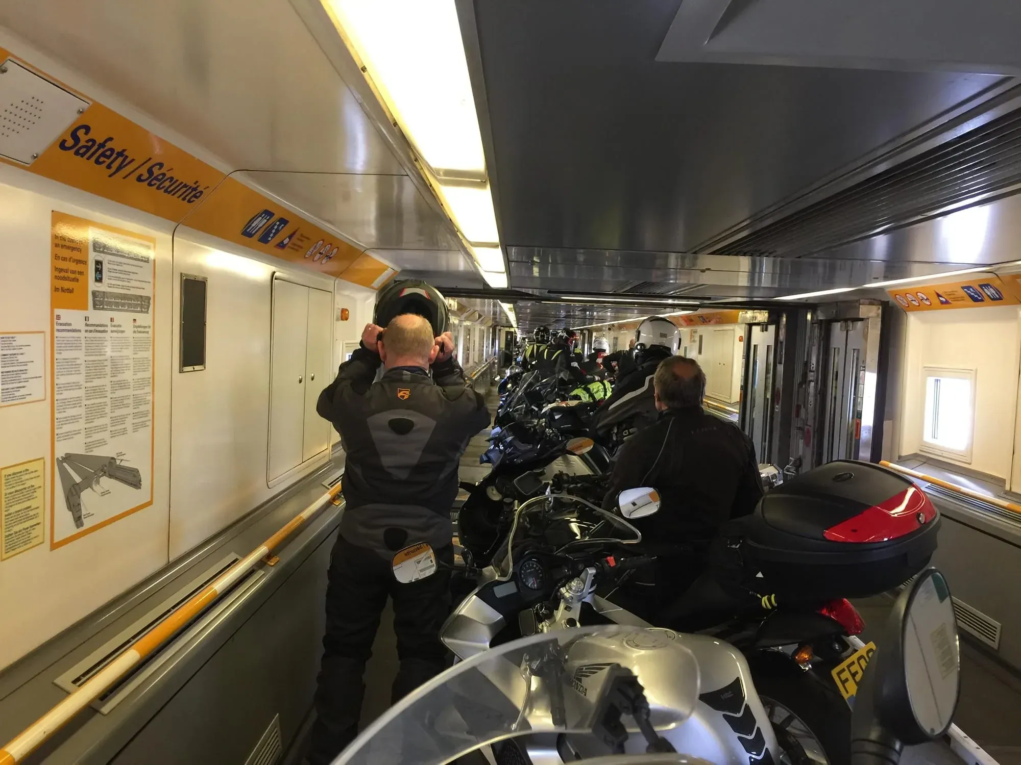 Motorcyclists inside train car with multiple bikes lined up for transport