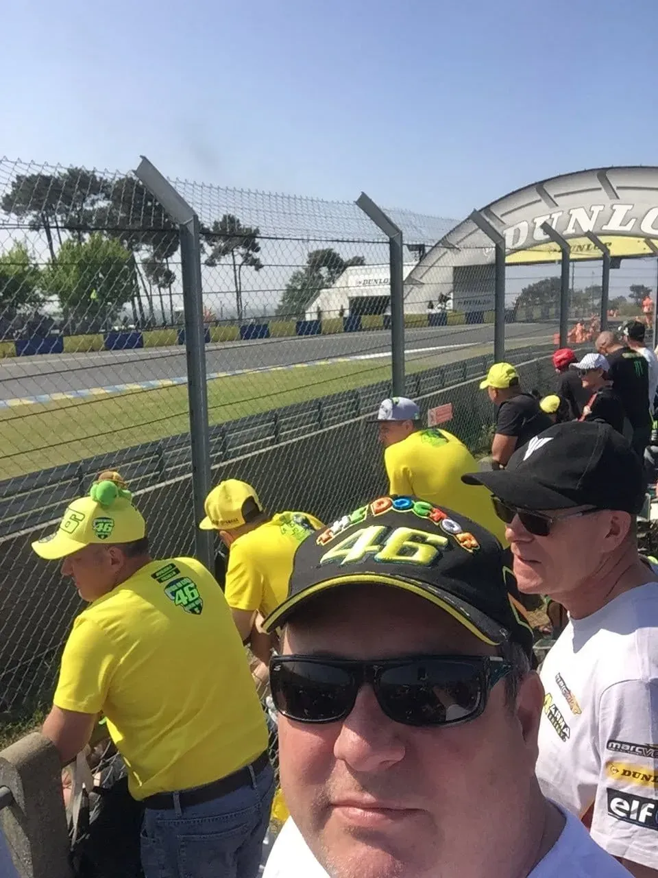 Spectators in yellow merchandise at racetrack viewing area near safety barriers