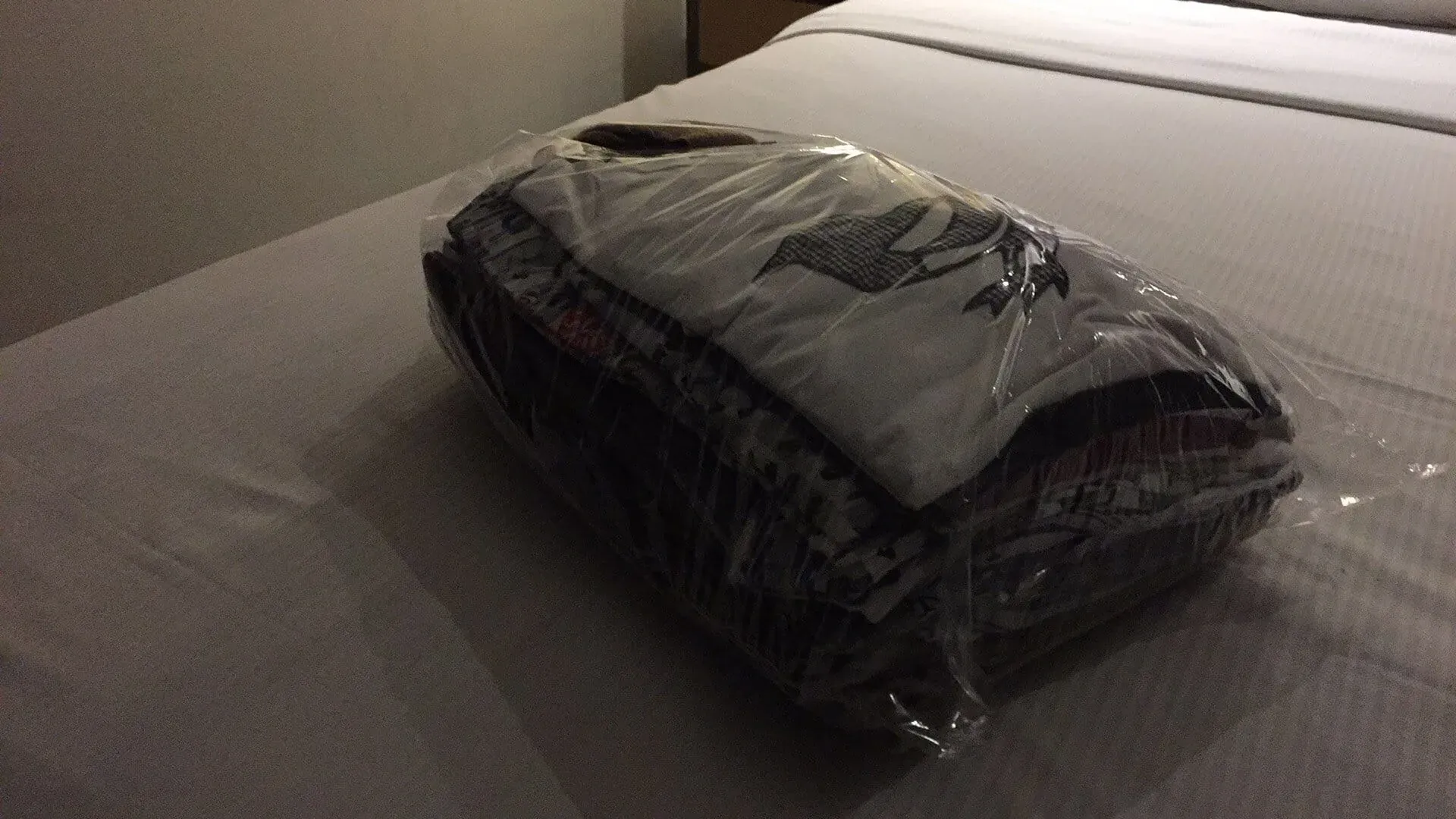 Packaged dark colored clothing or fabric wrapped in plastic on bed
