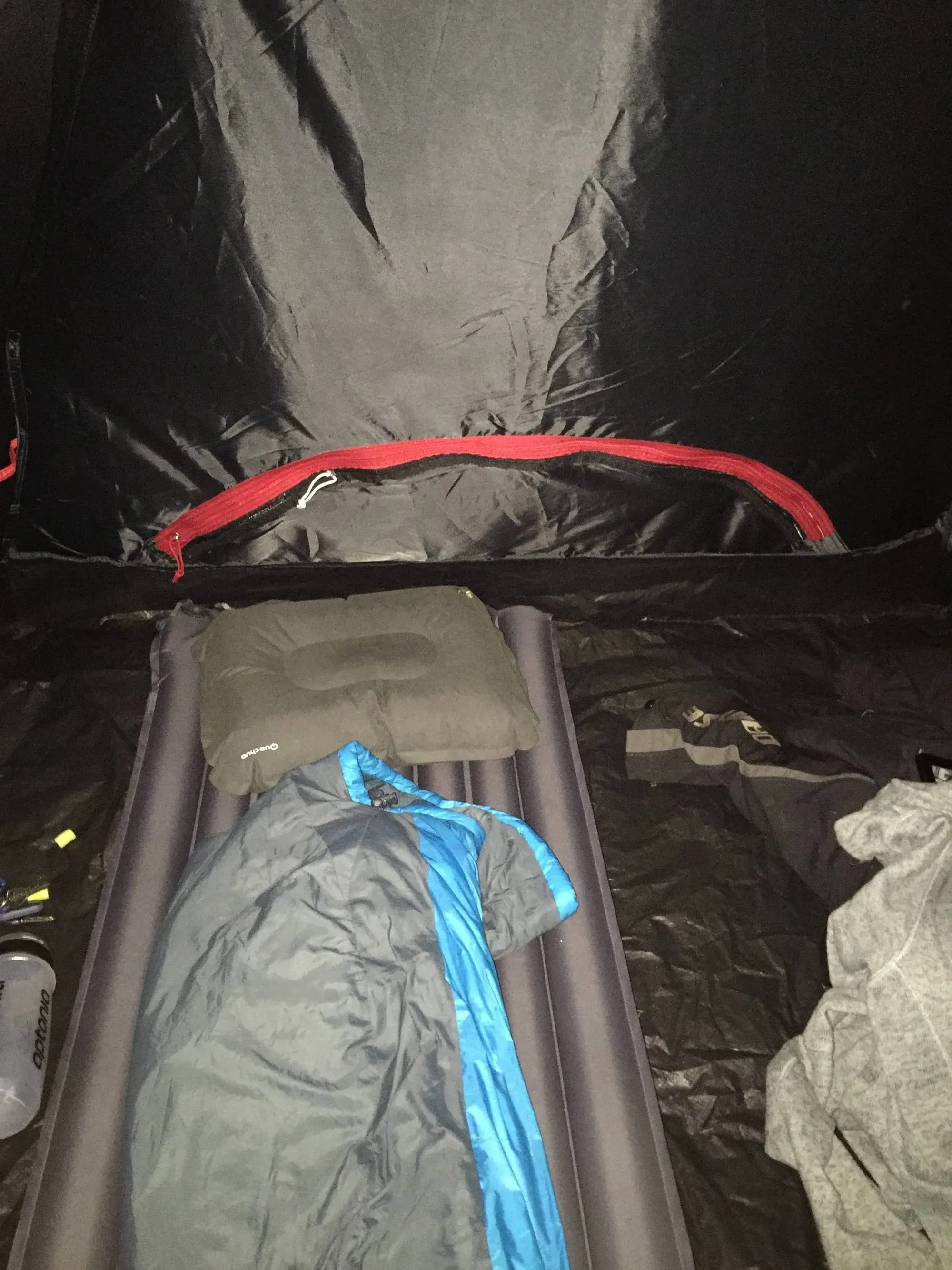 Inside tent showing blue sleeping bag on cot with camping gear and supplies