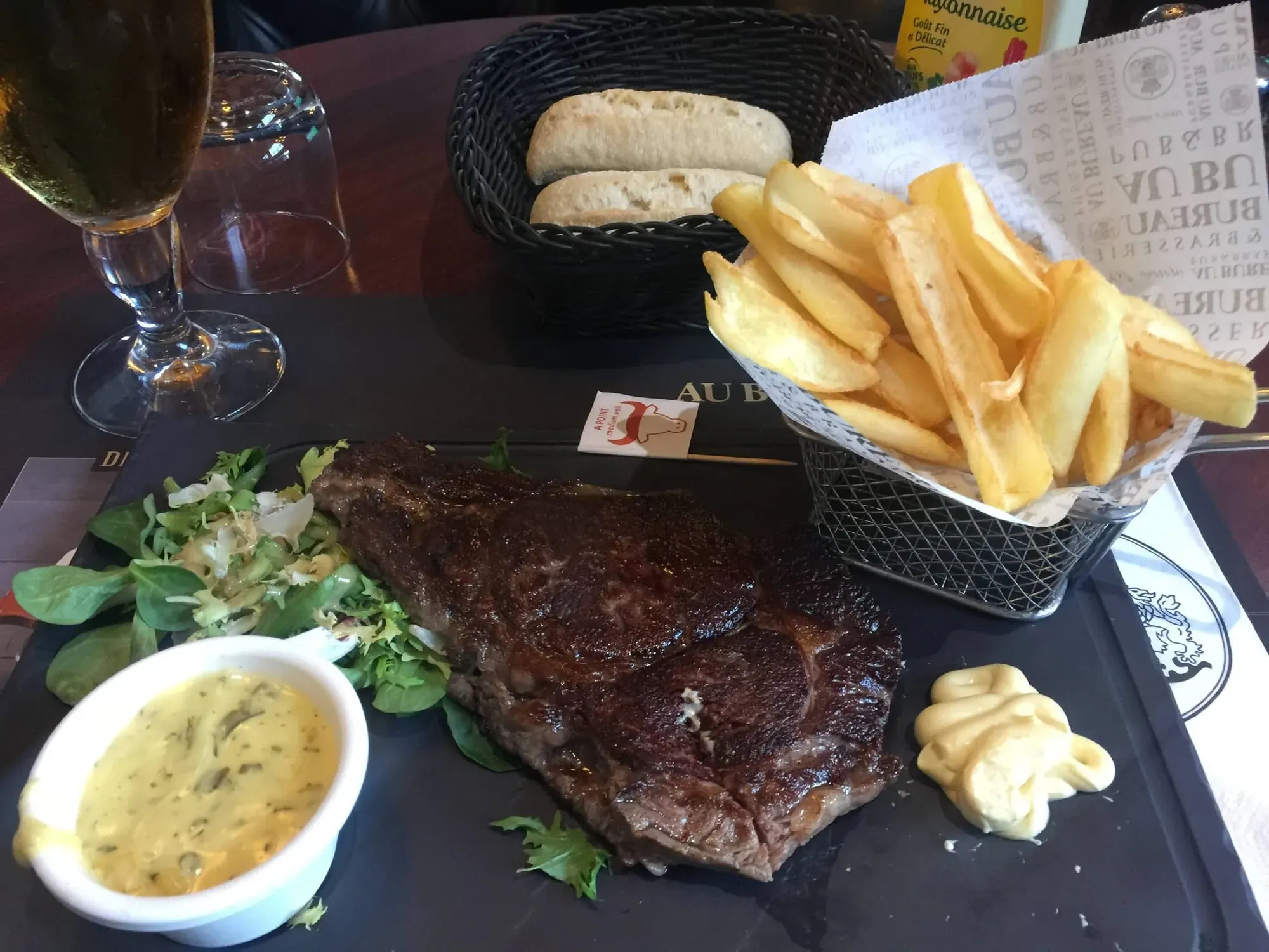 Steak dinner with fries, bread, sauce, and wine glass on table