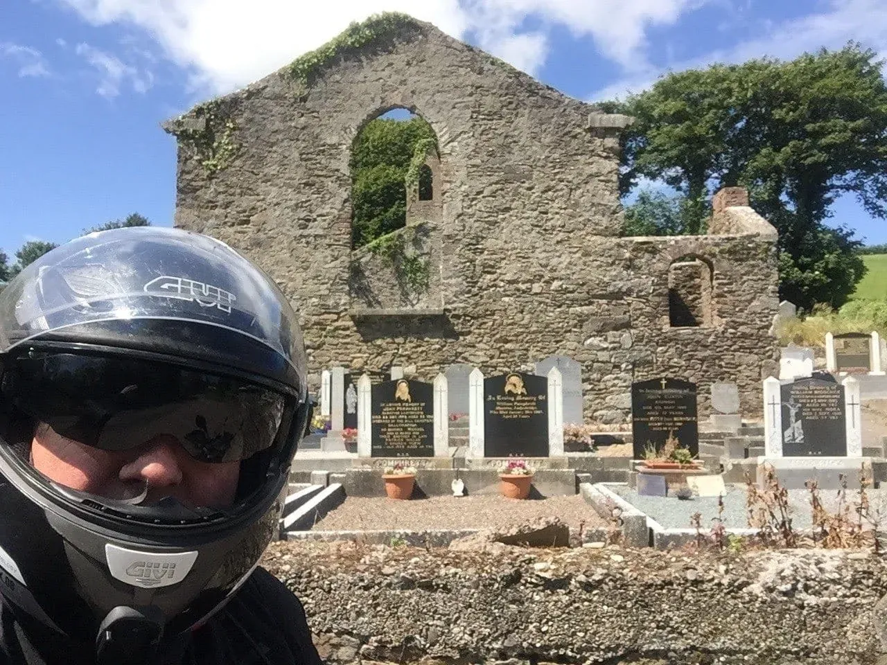 Black motorcycle helmet with ruined stone church and cemetery in background