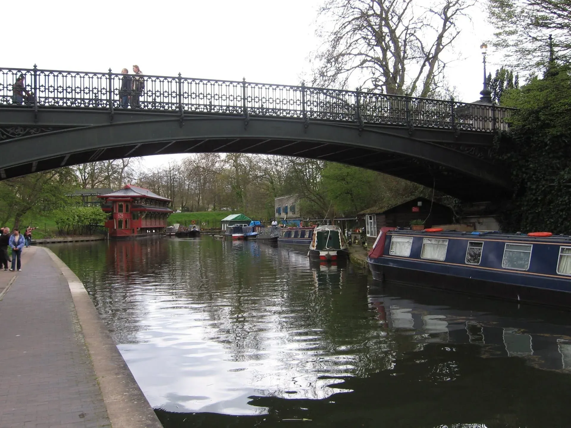 Arched bridge spanning canal with narrowboats moored below in tree-lined setting