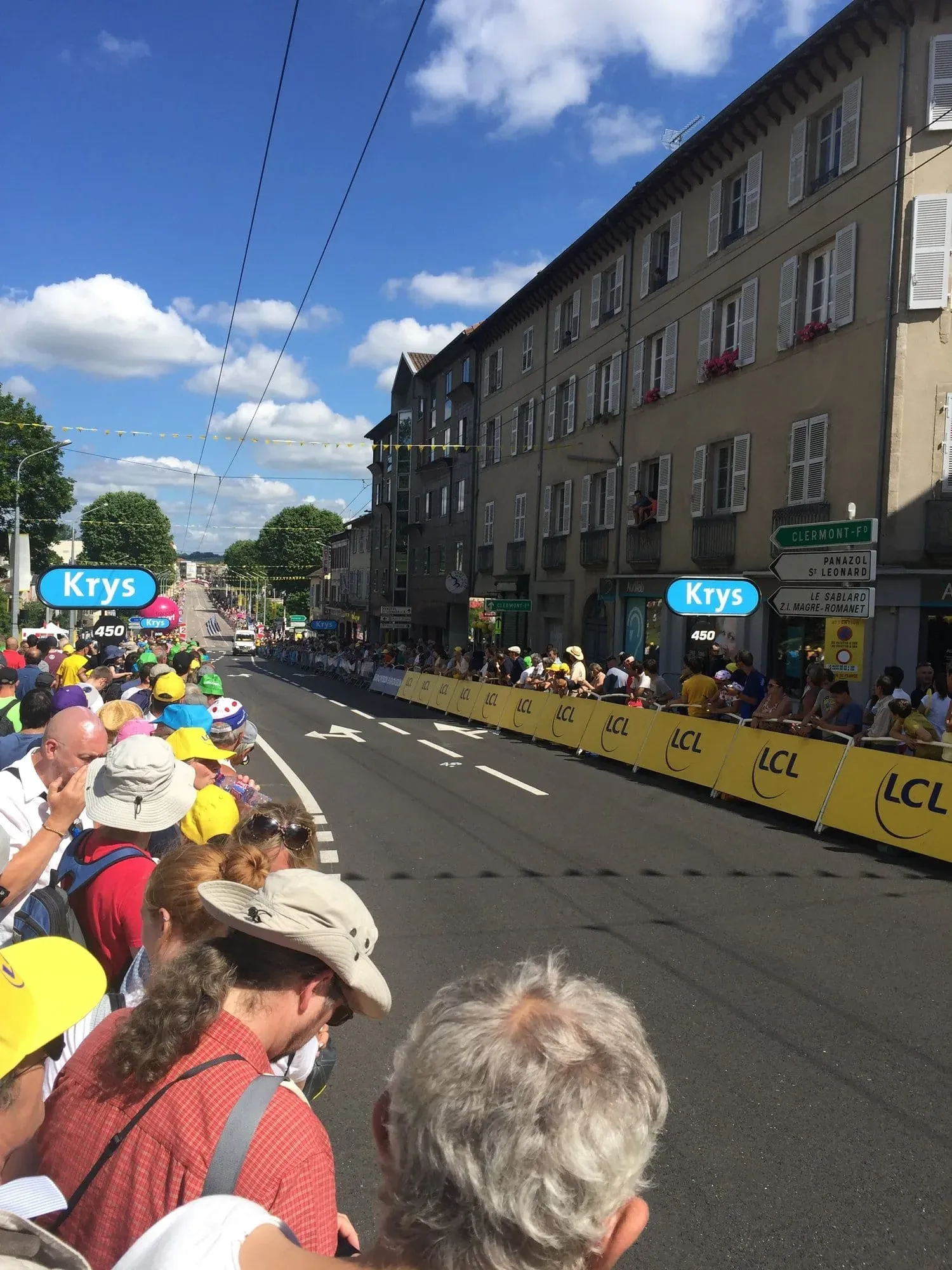 Spectators in yellow lining street watching Tour de France cyclists pass
