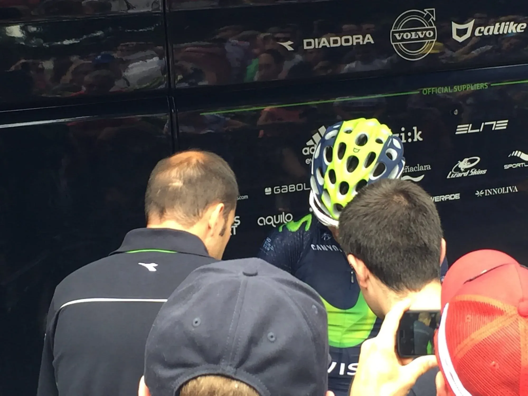 Cyclist wearing bright yellow helmet signs autographs by team bus