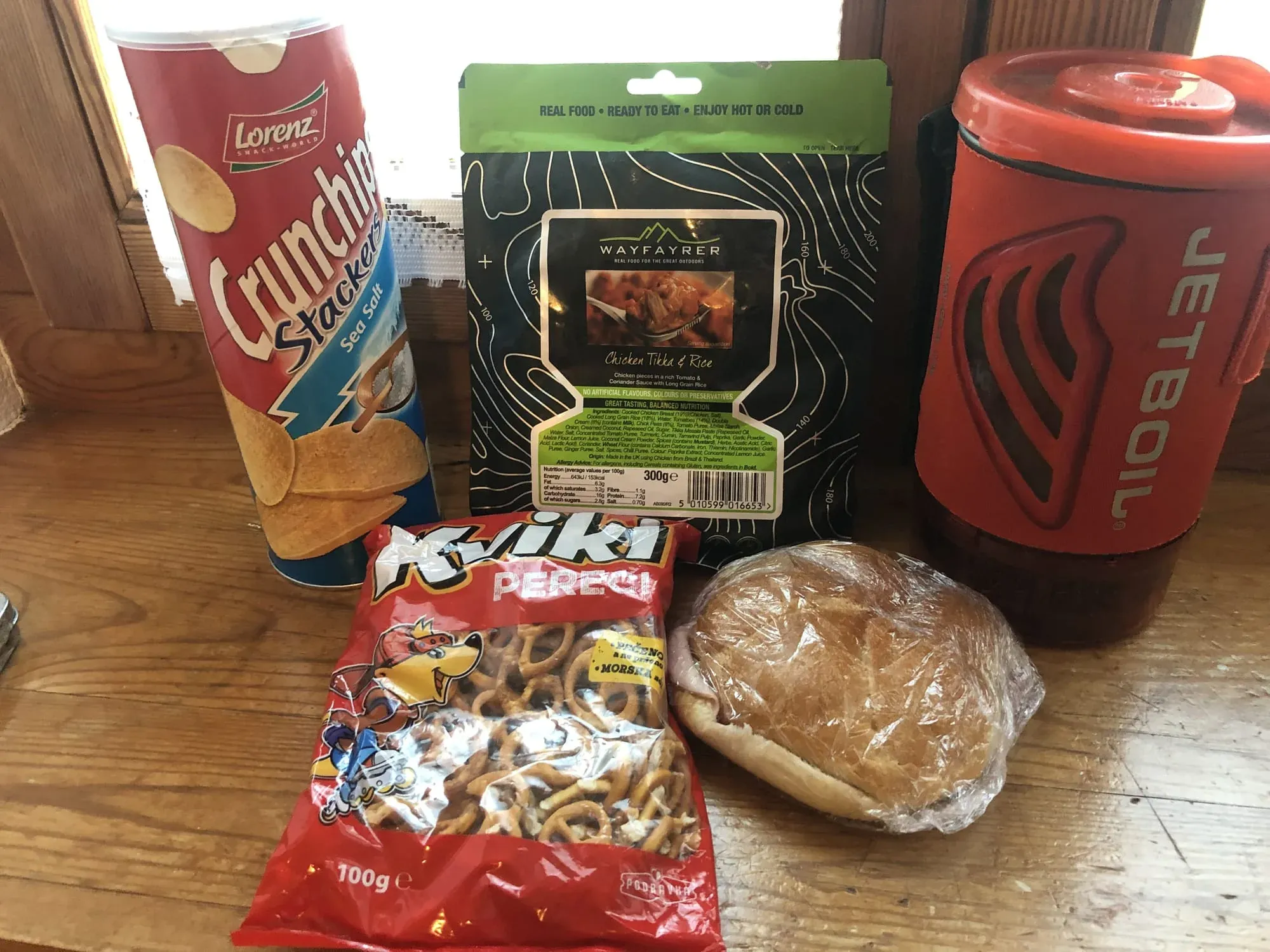Travel snacks and food items arranged on wooden surface including crisps and bread