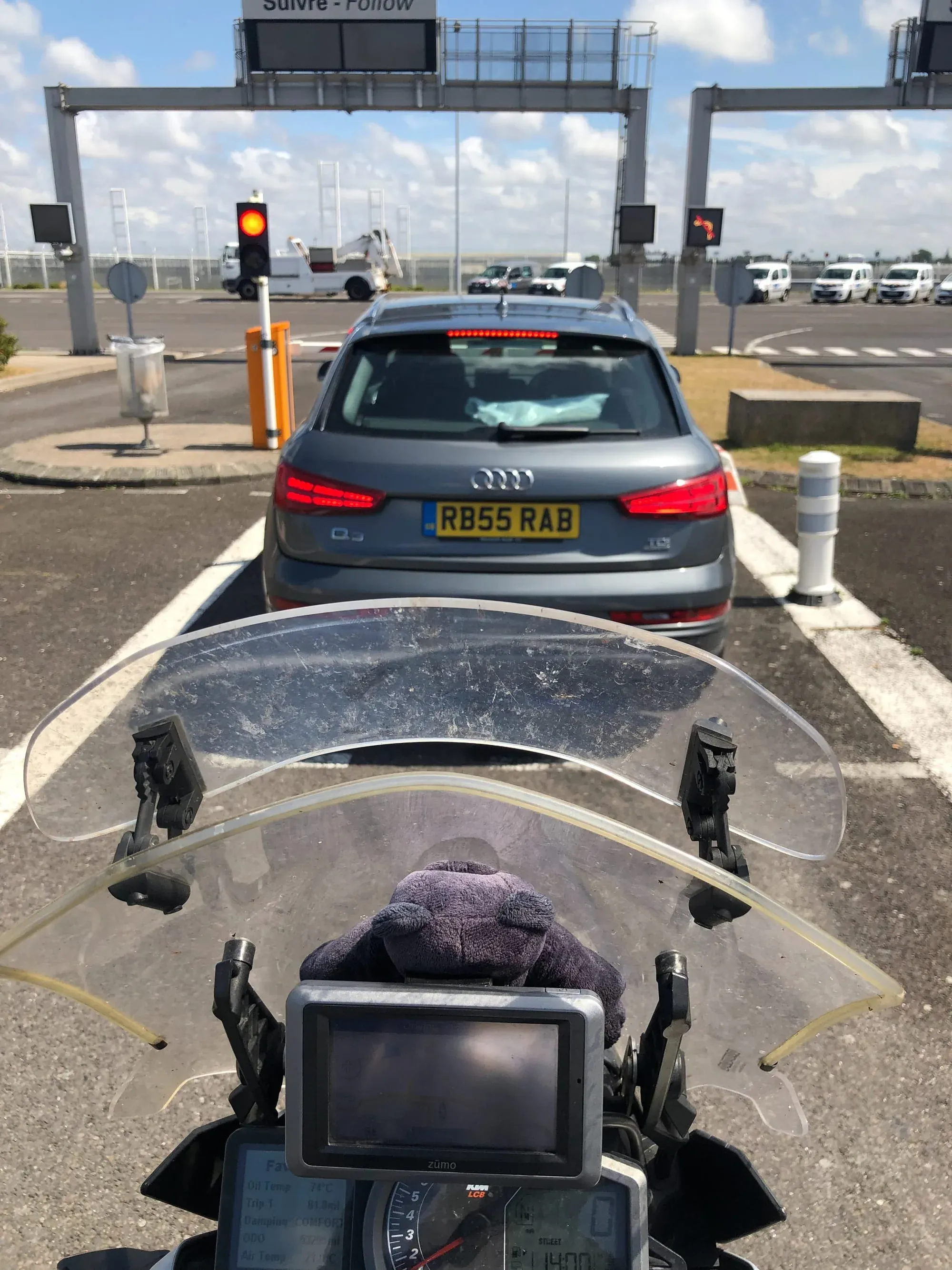 Motorcycle windscreen view of Audi at toll booth with yellow traffic light