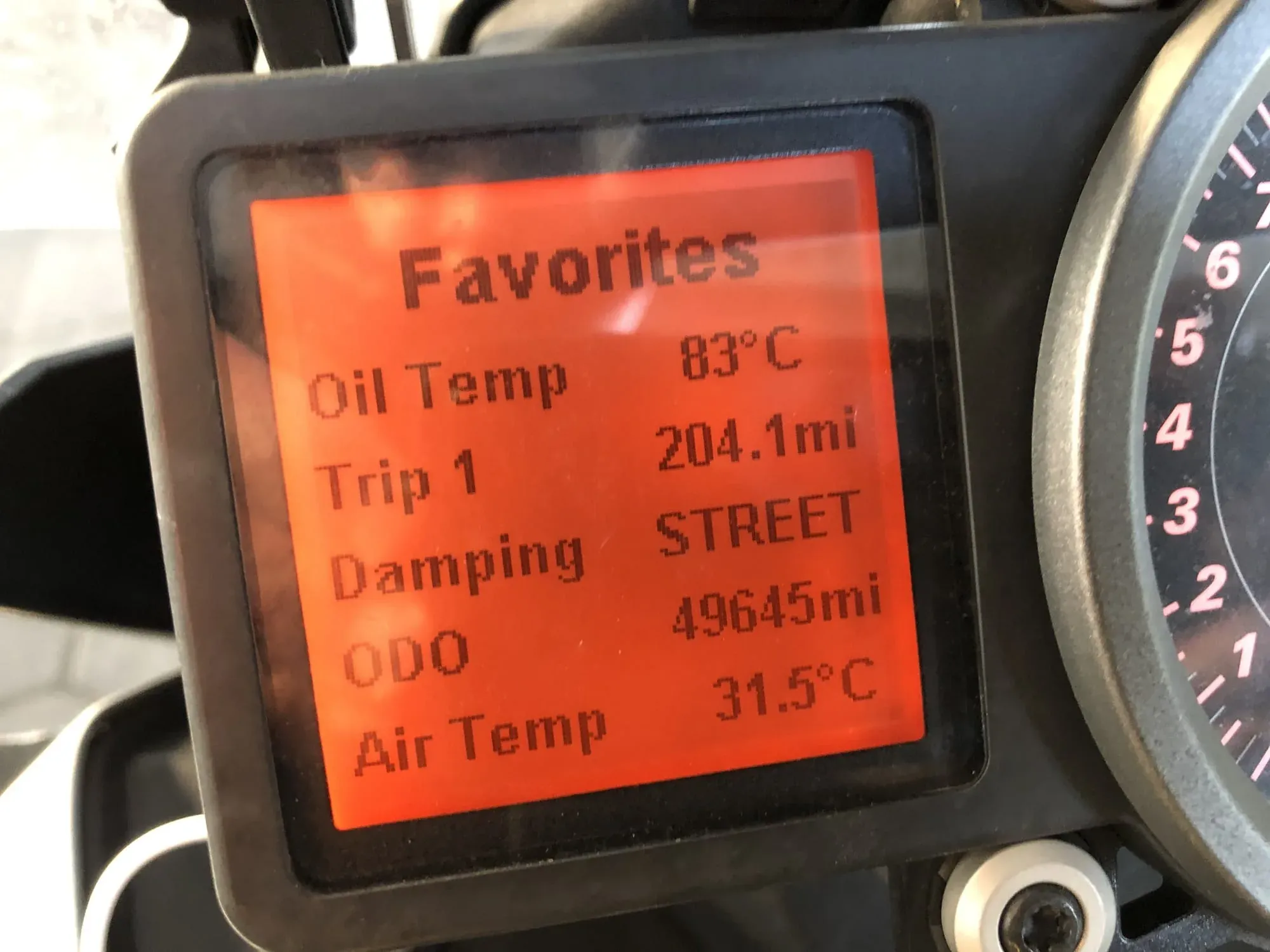 Motorcycle dashboard display showing oil temp, trip distance, and air temp