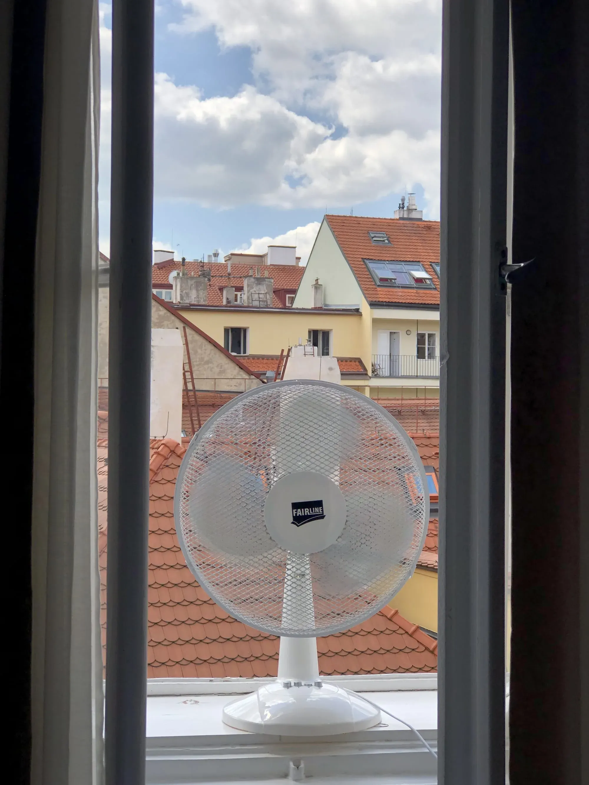 White desk fan on windowsill overlooking European rooftops and buildings