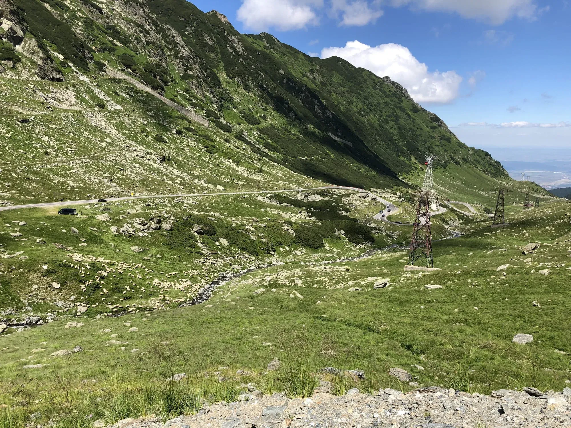 Mountain valley landscape with green slopes, road curves, and transmission tower