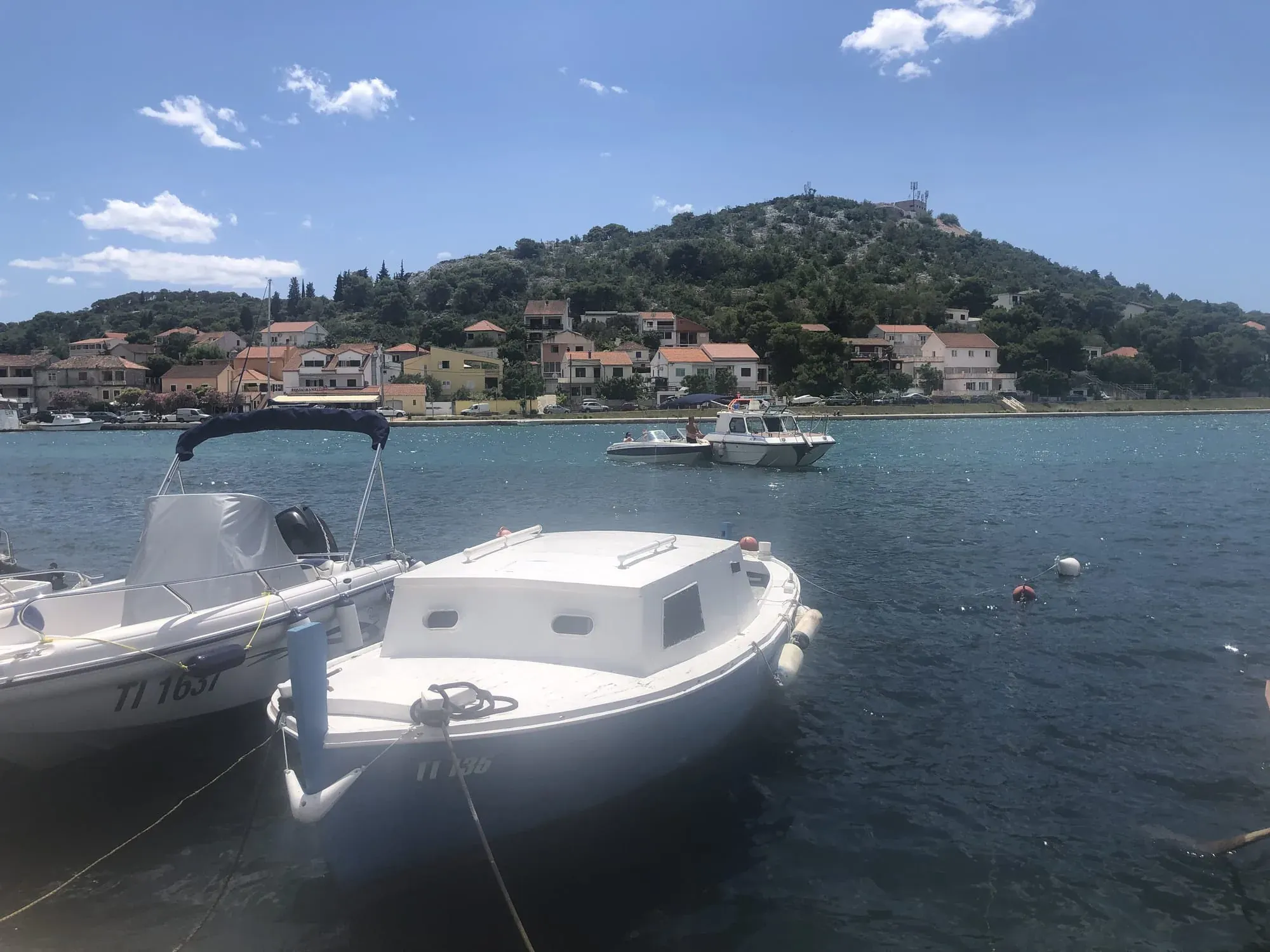 White motorboats moored in turquoise water with hillside village and green hills beyond