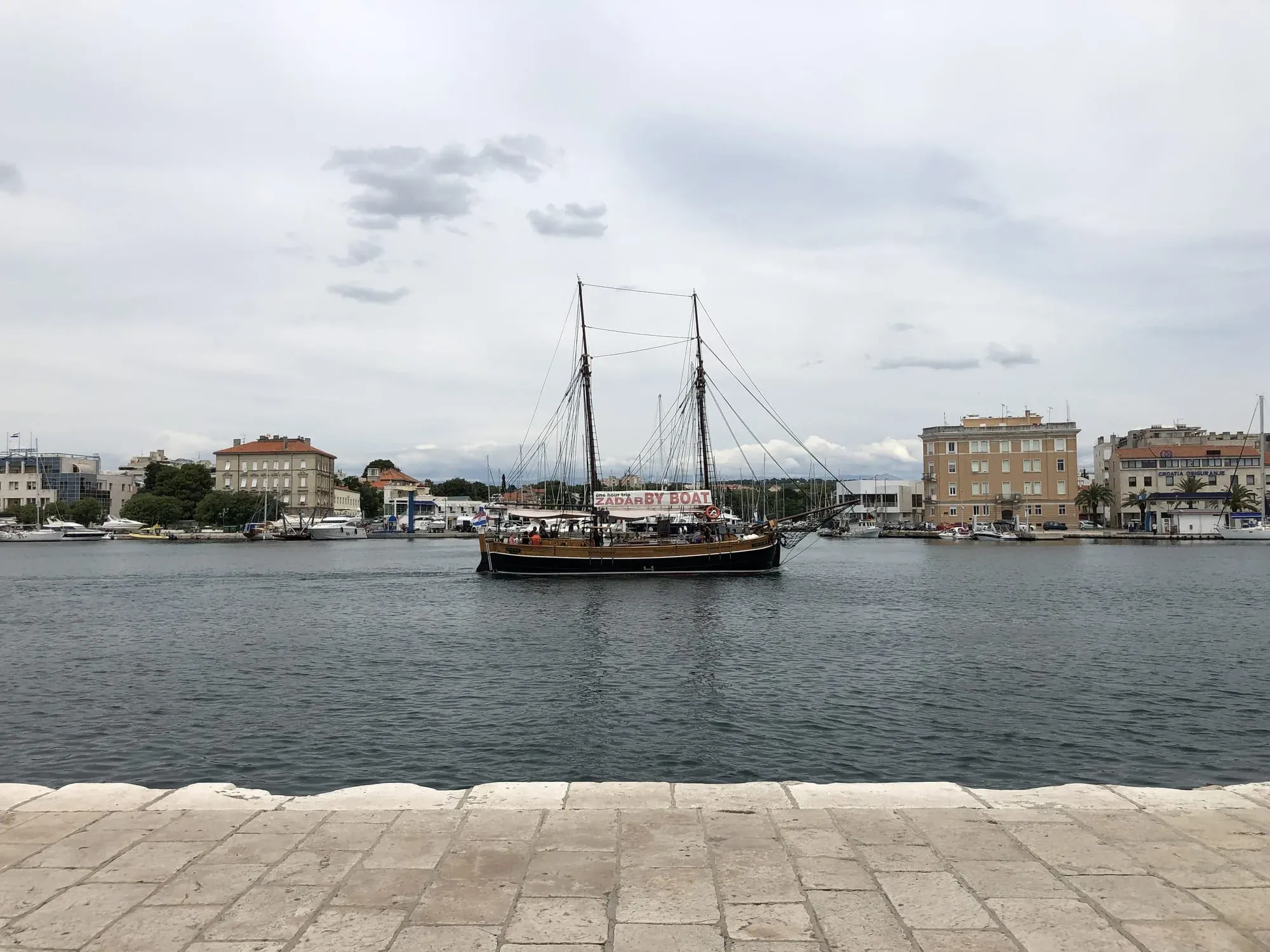 Traditional sailing ship with two masts in harbor surrounded by waterfront buildings