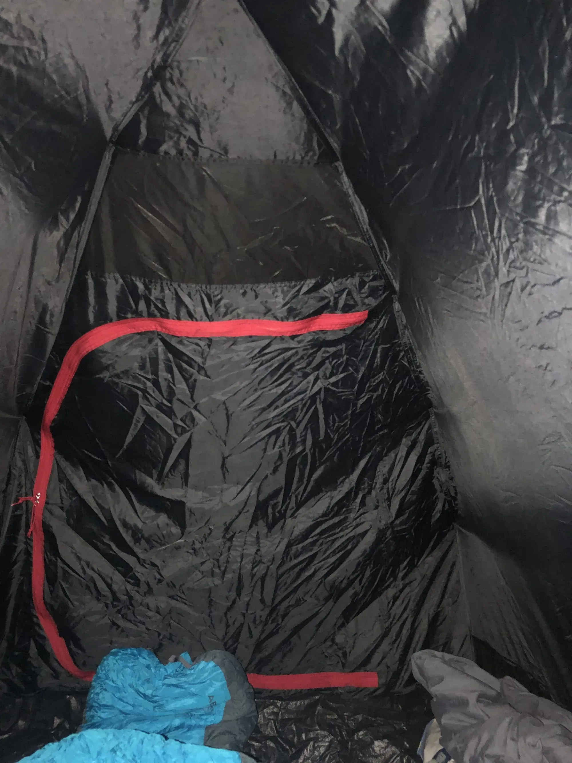 Black sleeping bag with red zipper detail and blue compression bag inside