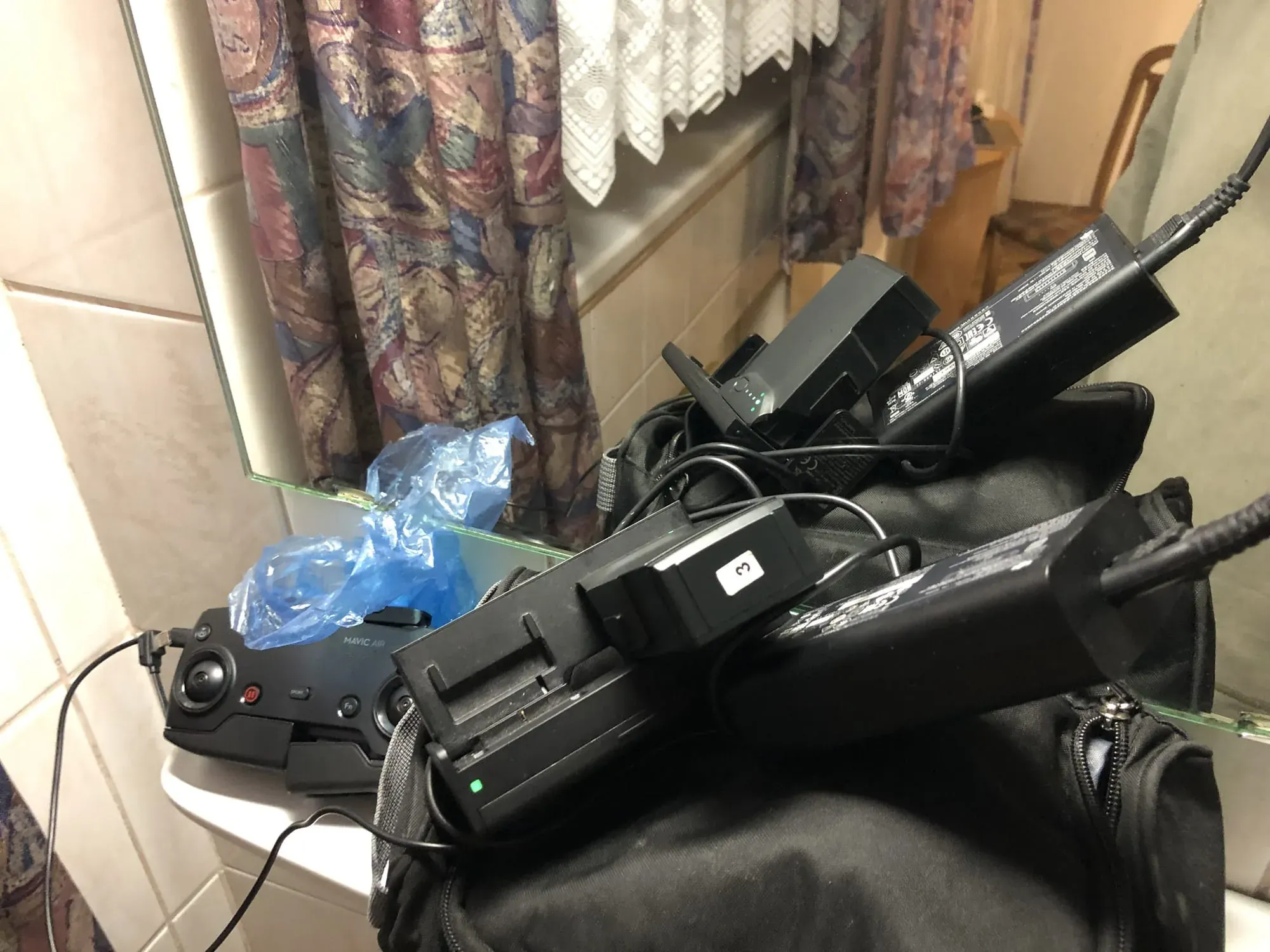 Drone controller and charger cables on table with patterned curtains behind