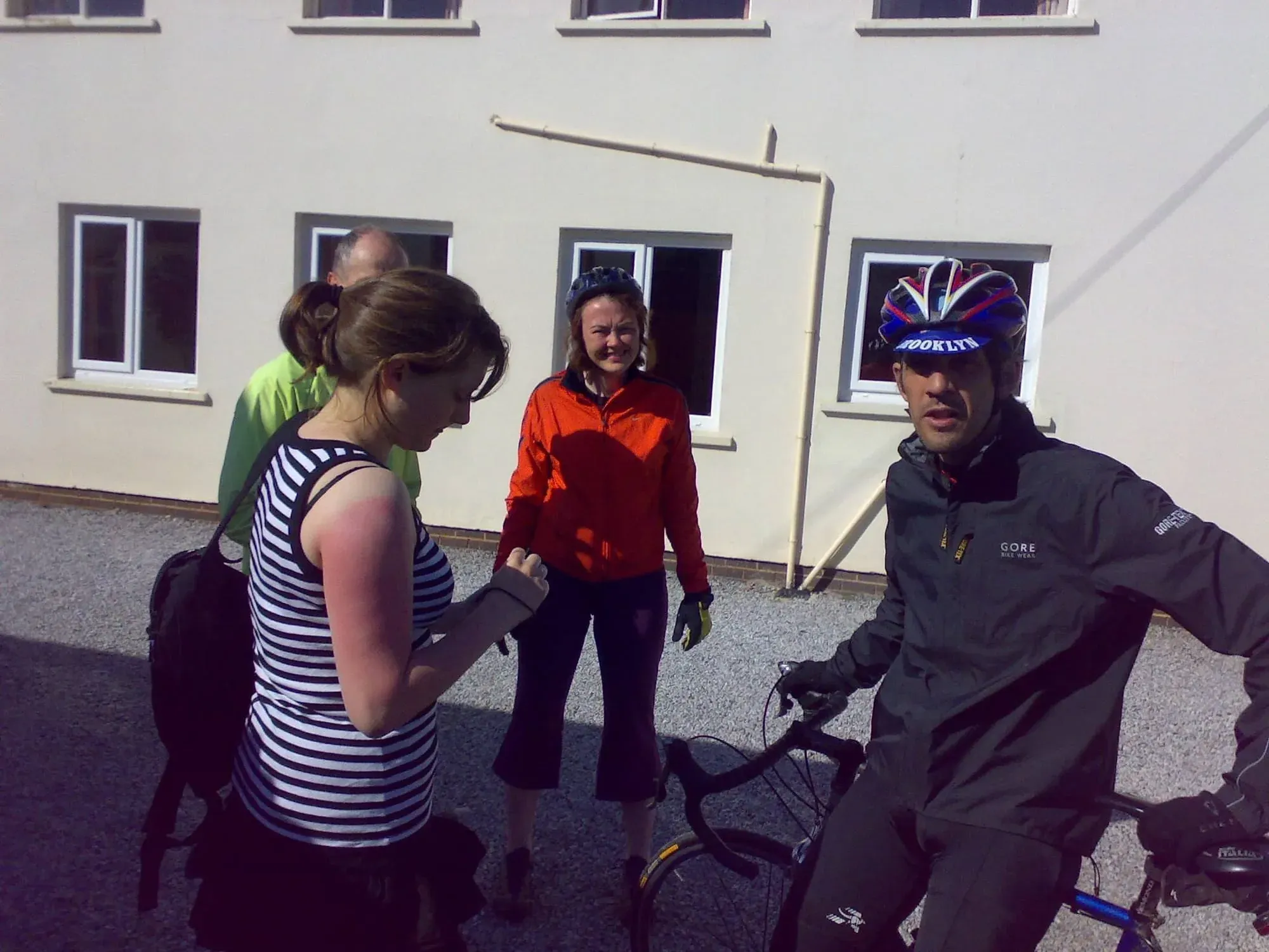 Cyclist in helmet speaking with woman in striped top outside a white building