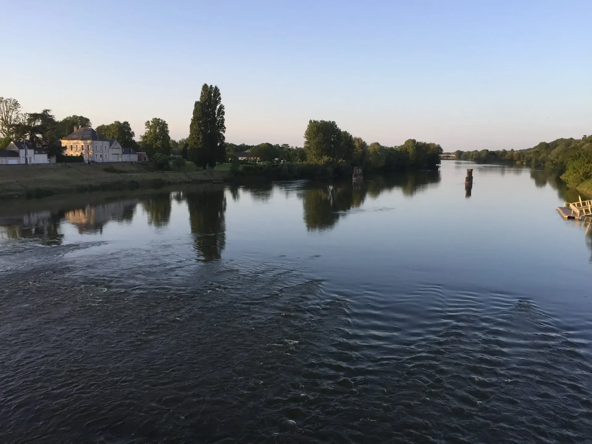 Riverside houses and trees reflected in calm water at La Ville-Sud