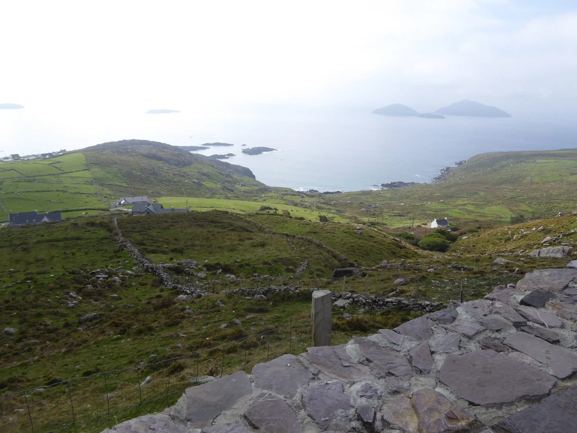 Panoramic valley view with green fields, stone walls, and distant coastline