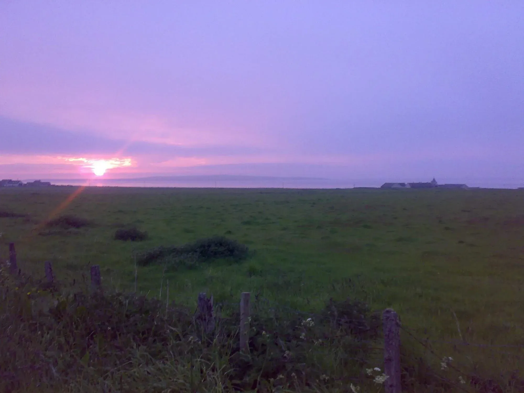 Purple sunset over flat countryside with fence posts in foreground