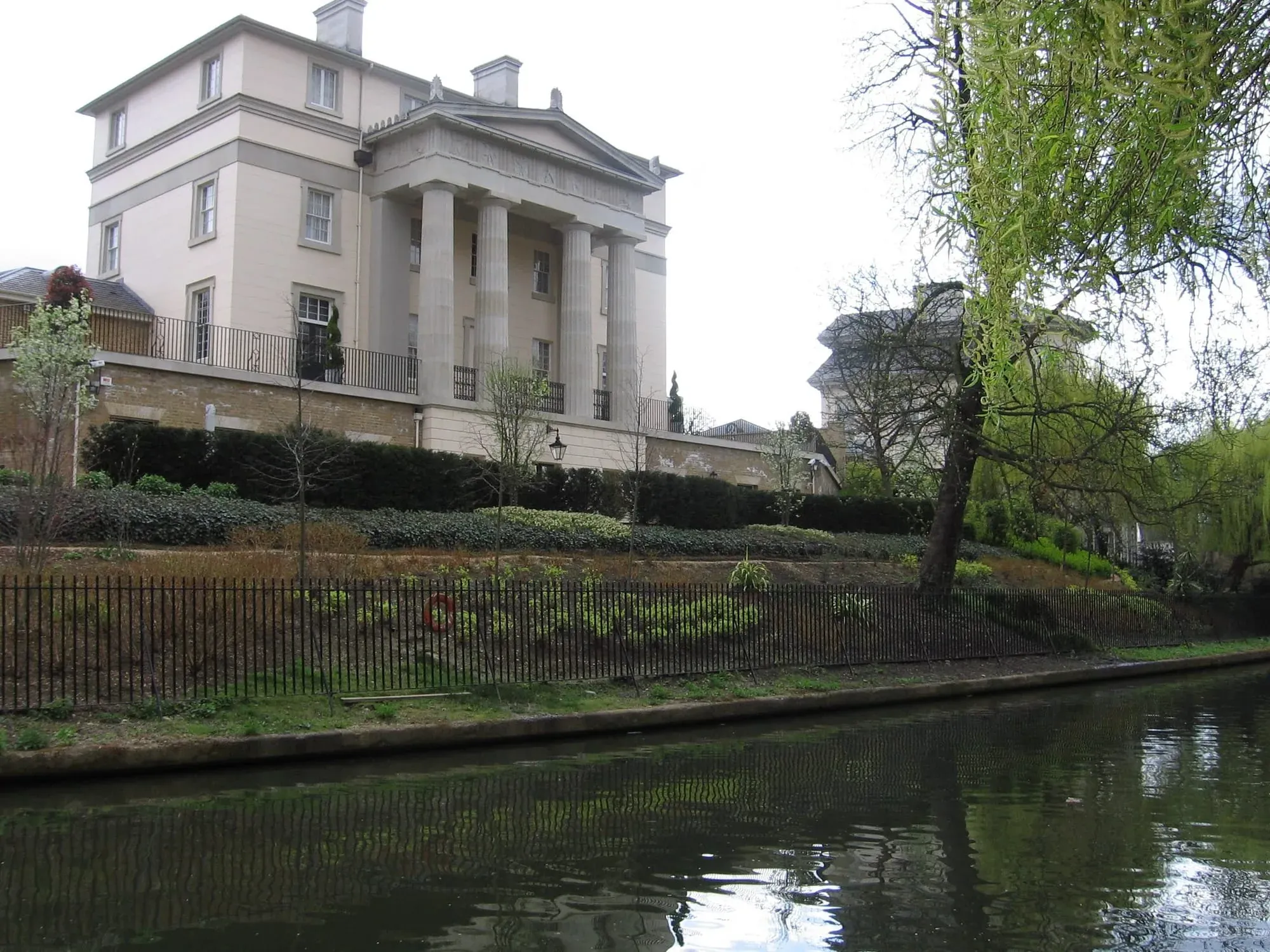 Classical stone house elevated on embankment beside canal with weeping willow
