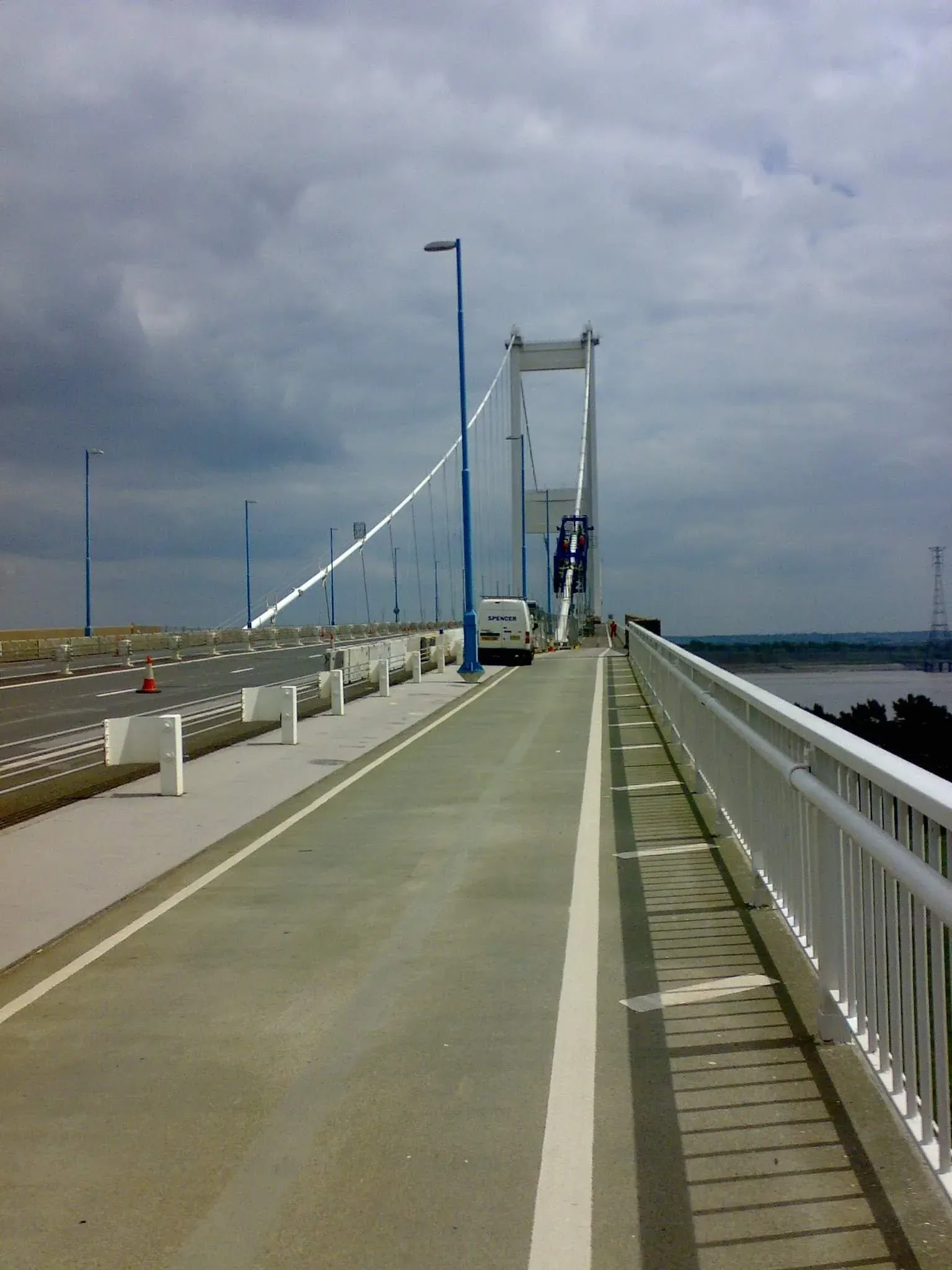 Pedestrian and cyclist on wide modern cable-stayed bridge spanning flat landscape with water below