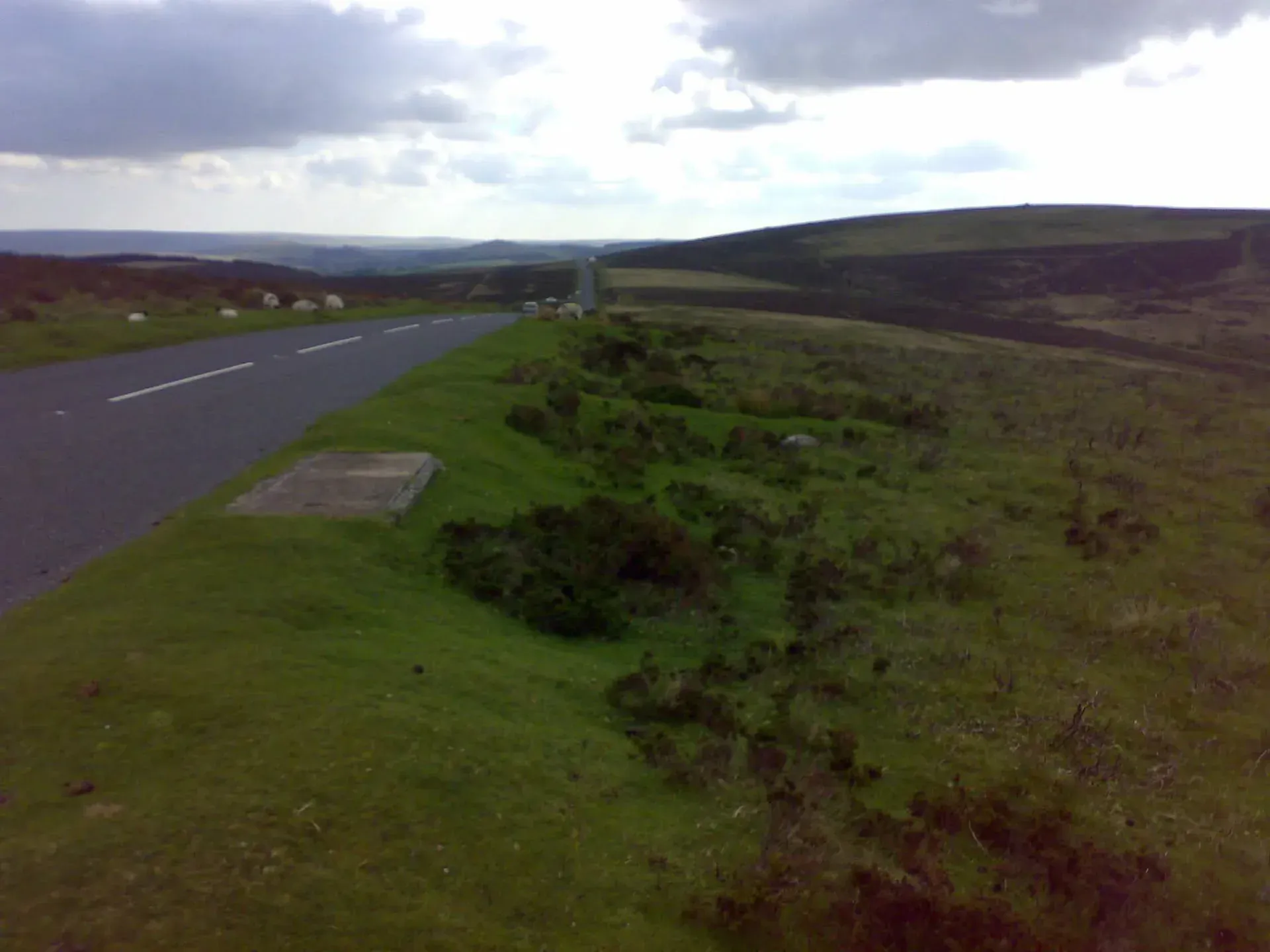 Road cutting through moorland hills with parked cars